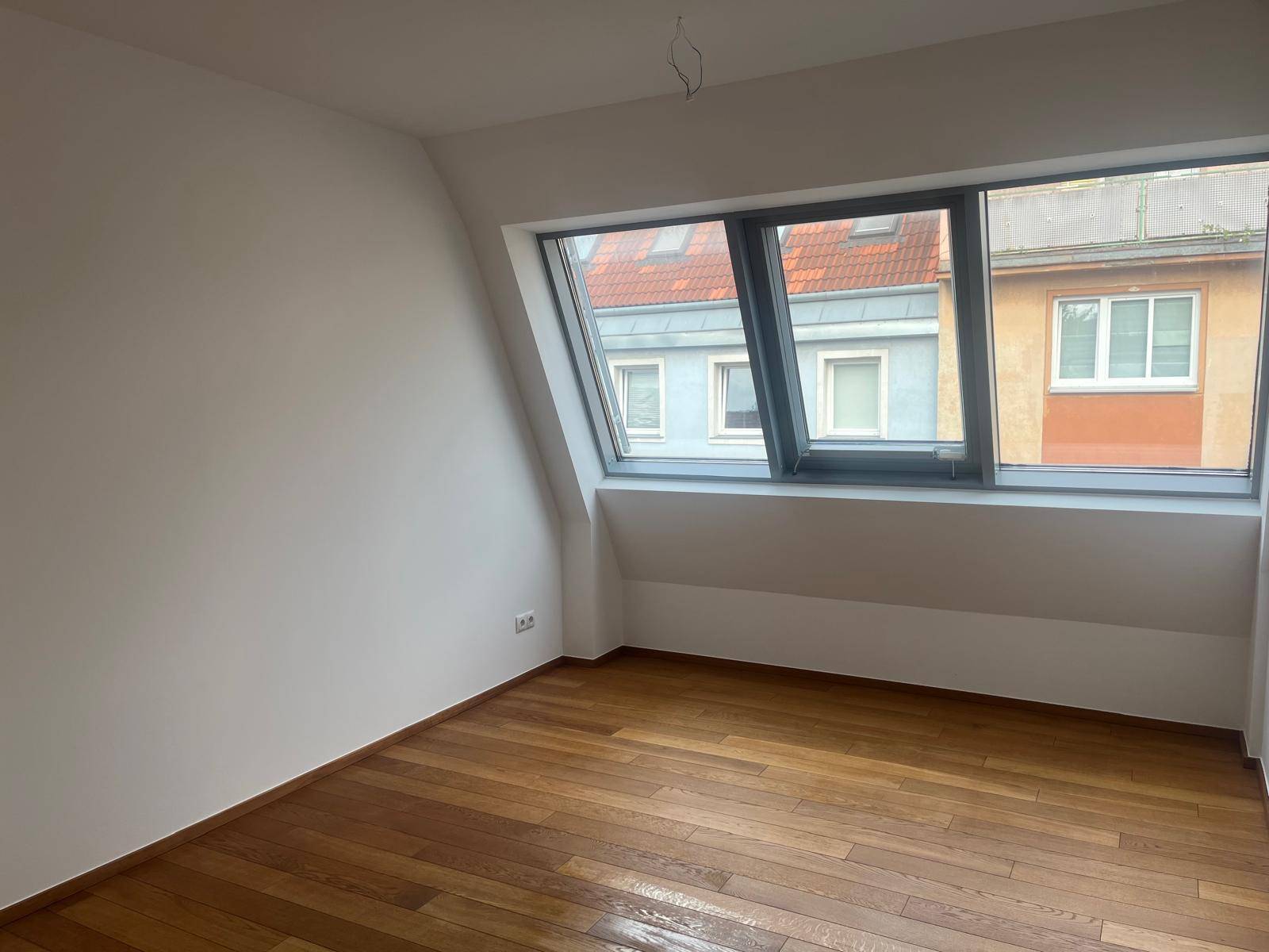 Geräumiges Zimmer mit Holzboden und großem Dachfenster, Blick auf die Stadt.