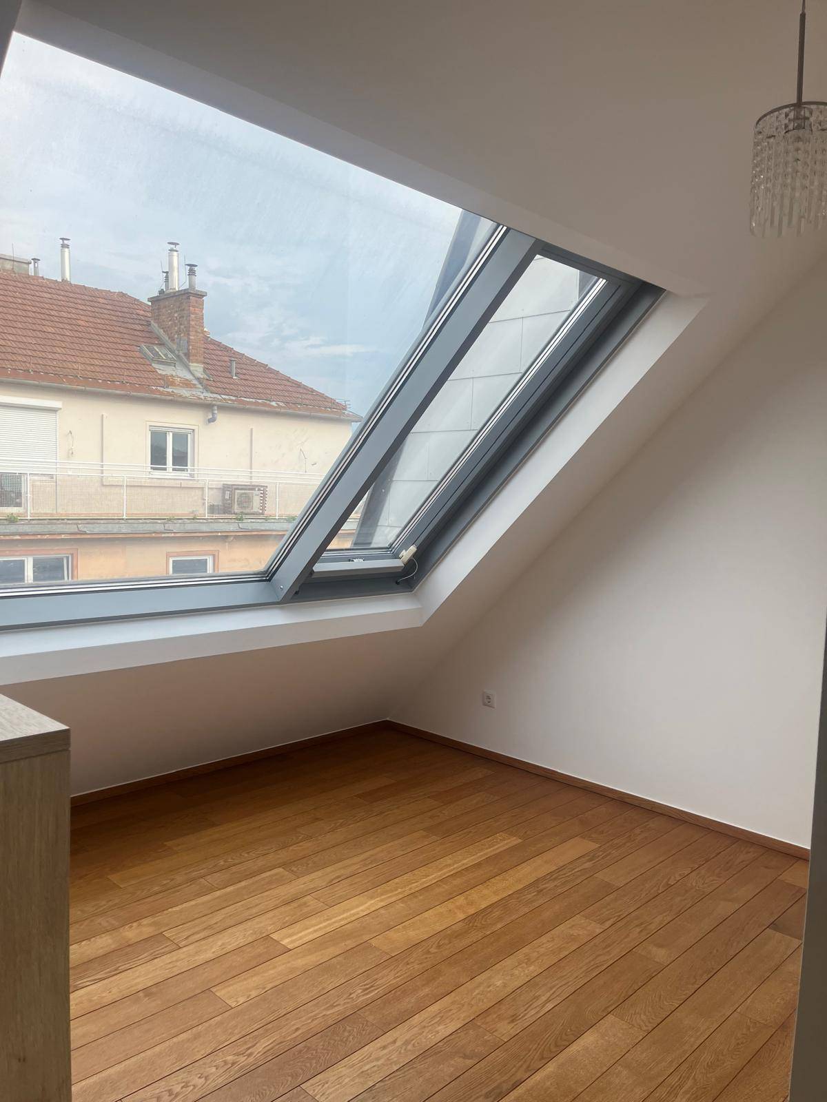 Geräumiges Zimmer mit Holzboden und großem Dachfenster, Blick auf die Umgebung.