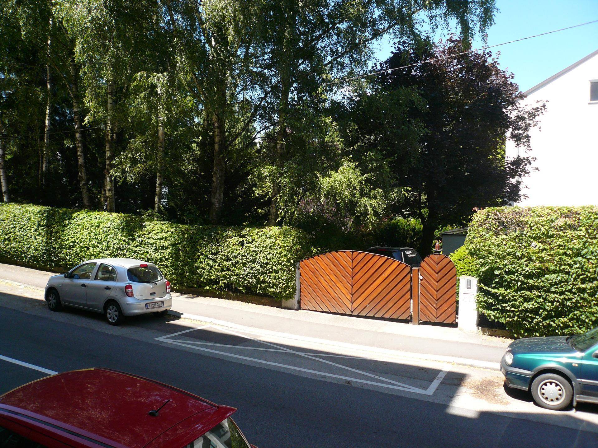 Außenansicht einer ruhigen Straße mit gepflegter Hecke und Holztor zur Einfahrt.