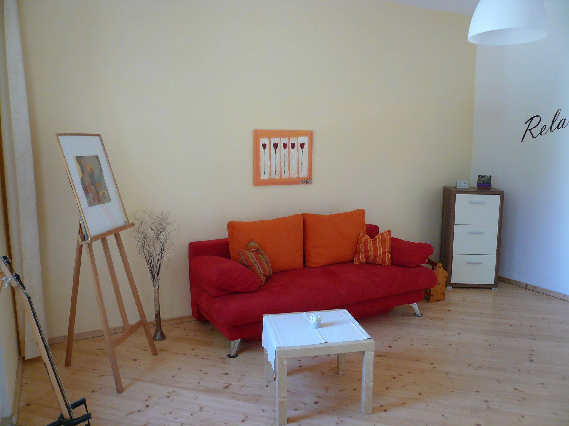 Gemütliches Wohnzimmer mit rotem Sofa, Holzboden und moderner Dekoration an der Wand.