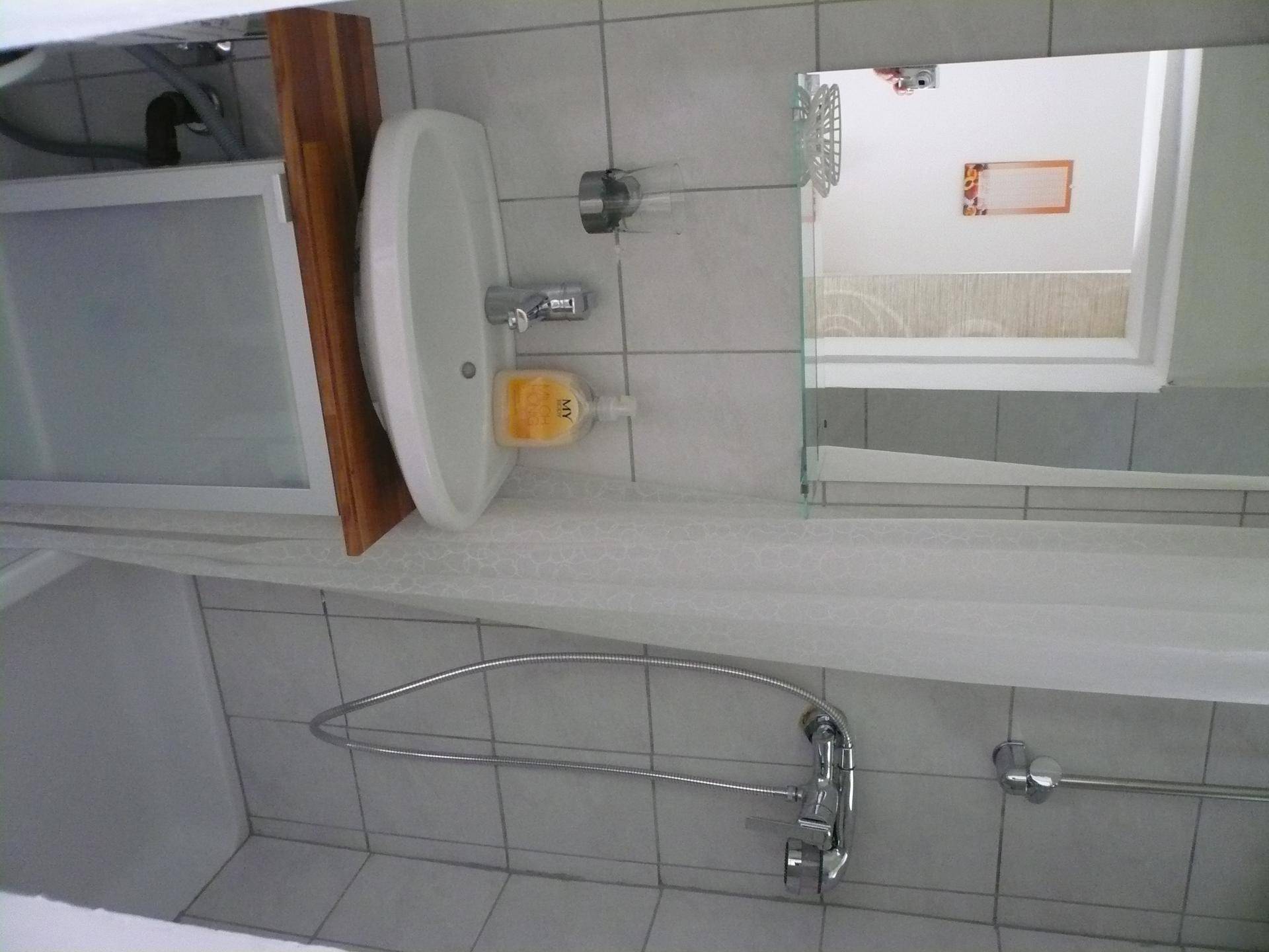 Helles Badezimmer mit Waschbecken, Spiegel und Duschbereich, gefliest in Weiß.