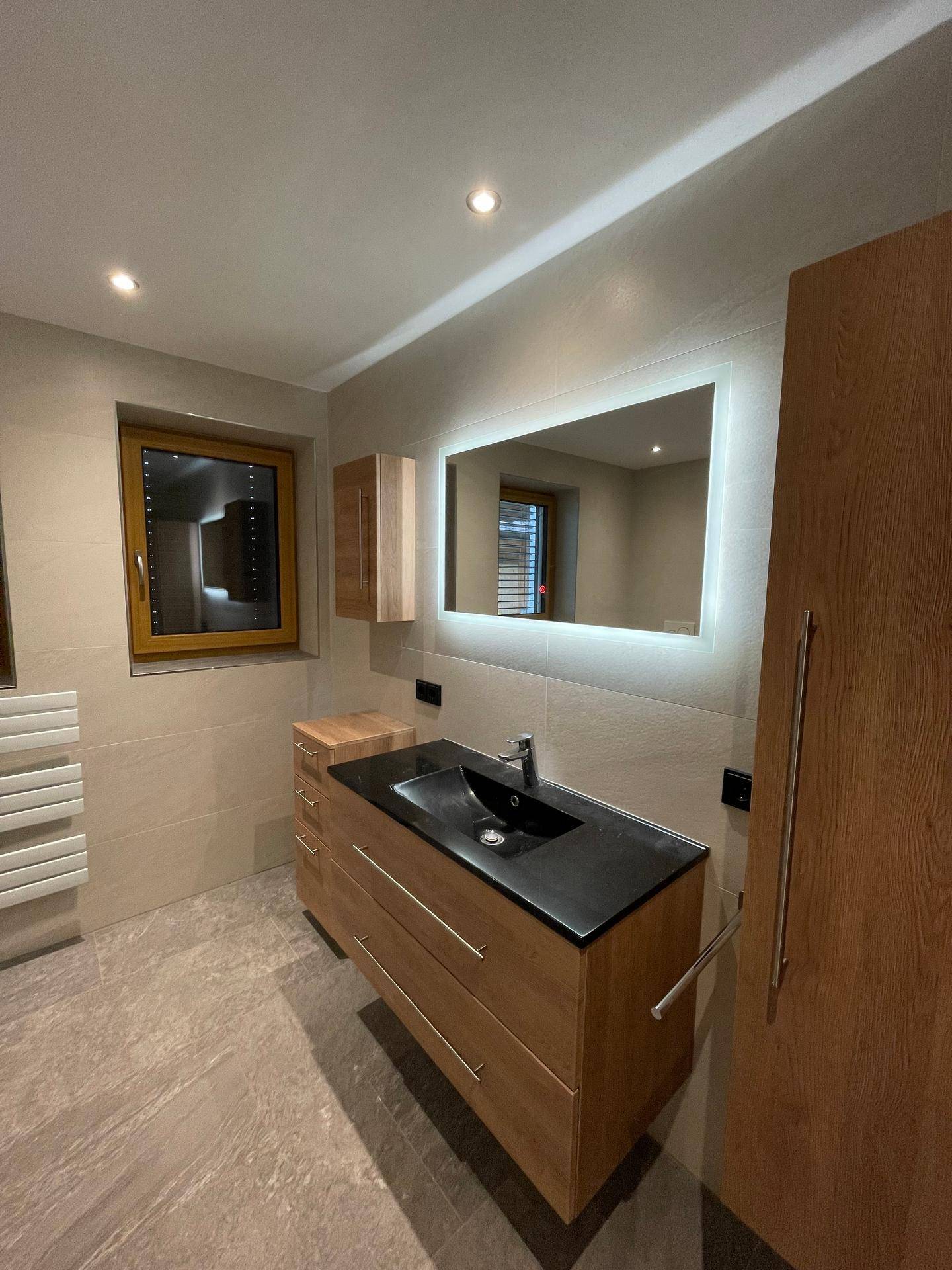 Modernes Badezimmer mit Holzwaschtisch, beleuchtetem Spiegel und praktischem Handtuchheizkörper.