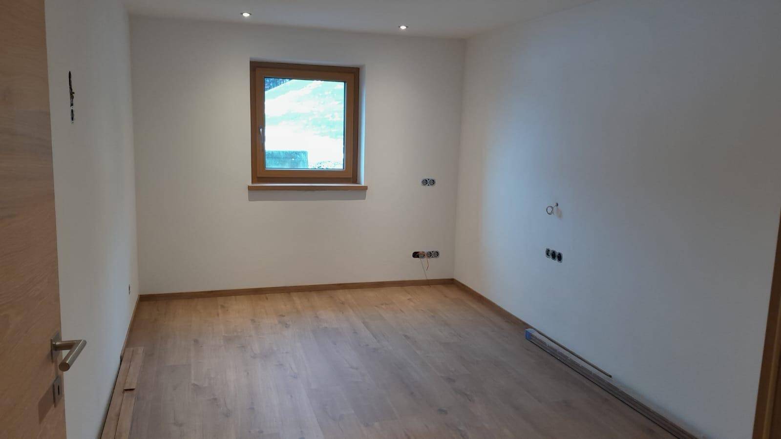 Leeres Zimmer mit Holzboden und Fenster, bereit für die individuelle Gestaltung.