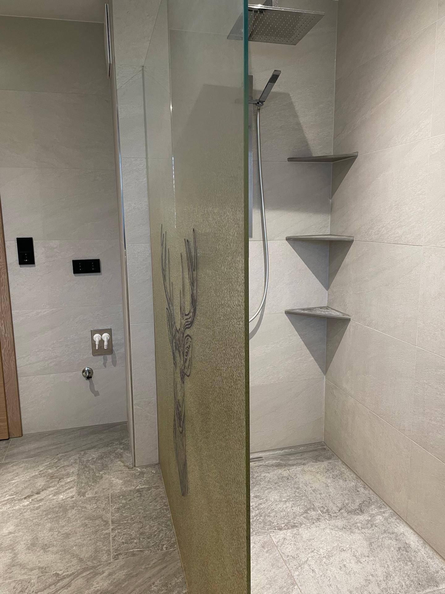 Geräumige begehbare Dusche mit Regenduschkopf und modernen grauen Fliesen.