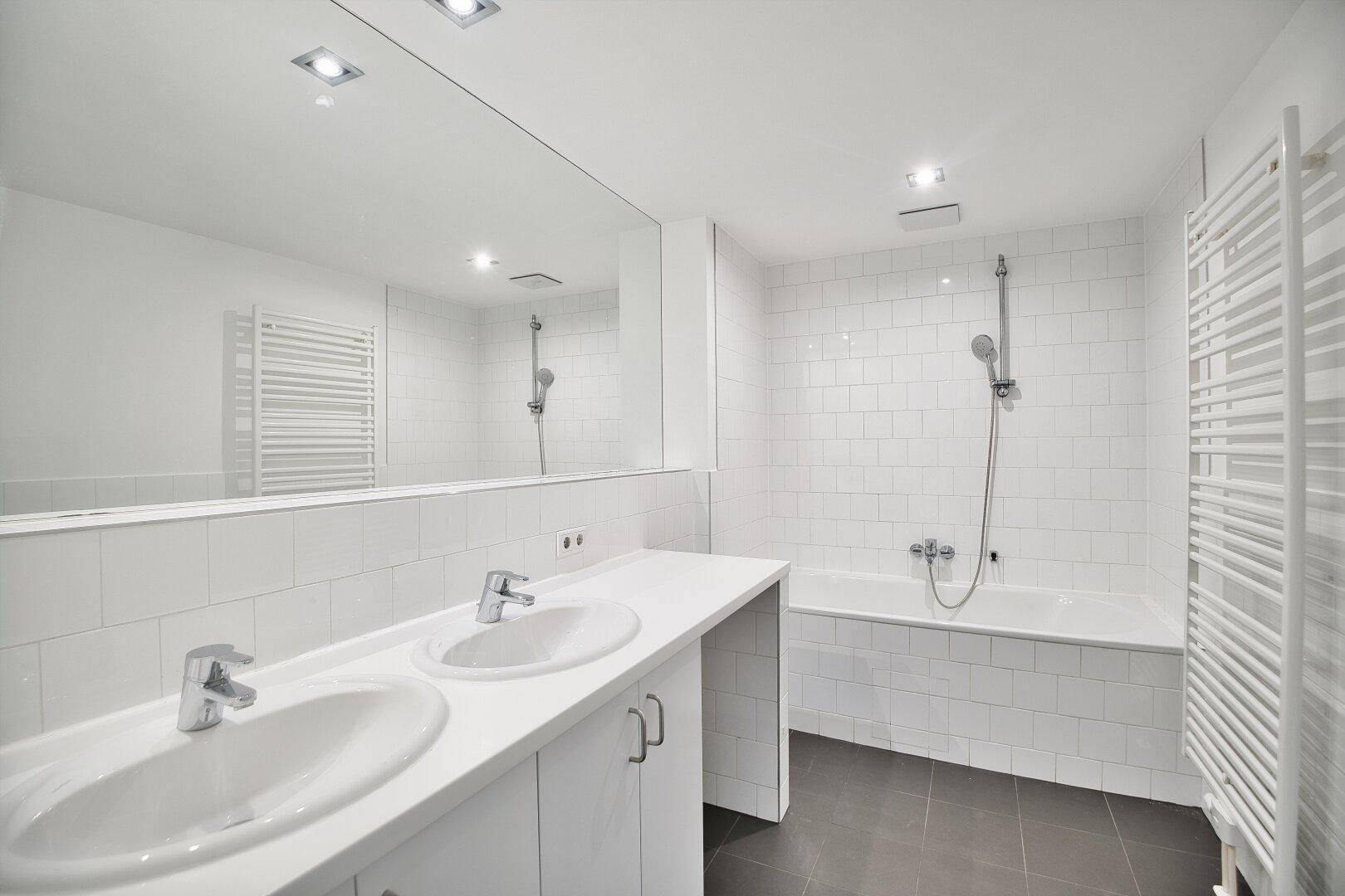 Modernes Badezimmer mit weißen Fliesen, Doppelwaschbecken, Badewanne und beheiztem Handtuchhalter.