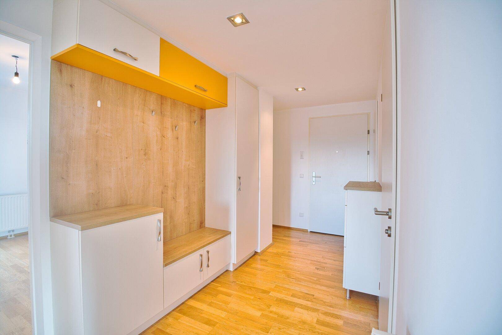 Heller Eingangsbereich mit maßgefertigten Holzmöbeln, Sitzbank und Stauraum, sowie Parkettboden.