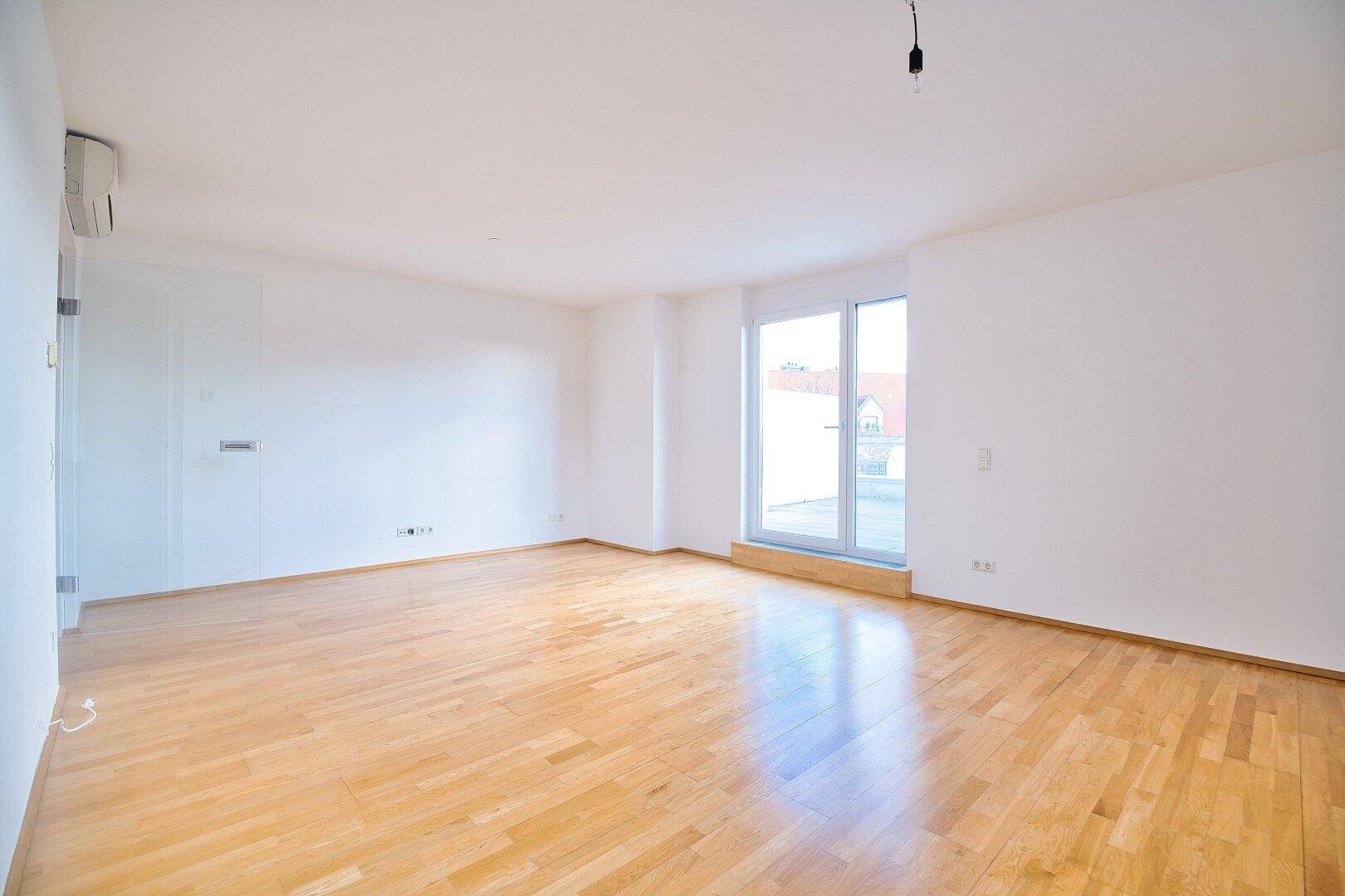 Geräumiges Wohnzimmer mit hellem Parkettboden und großer Fensterfront für viel Tageslicht.