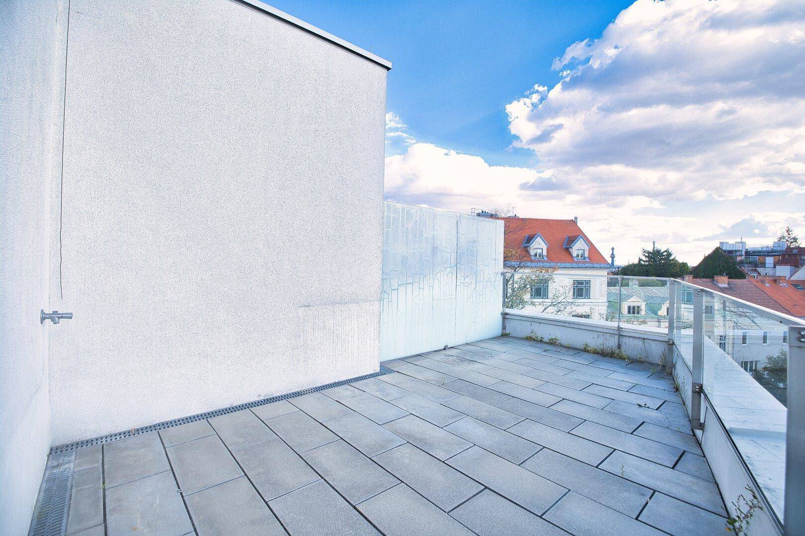 Geräumige Dachterrasse mit modernen Fliesen und Glasgeländer, bietet einen weiten Blick.