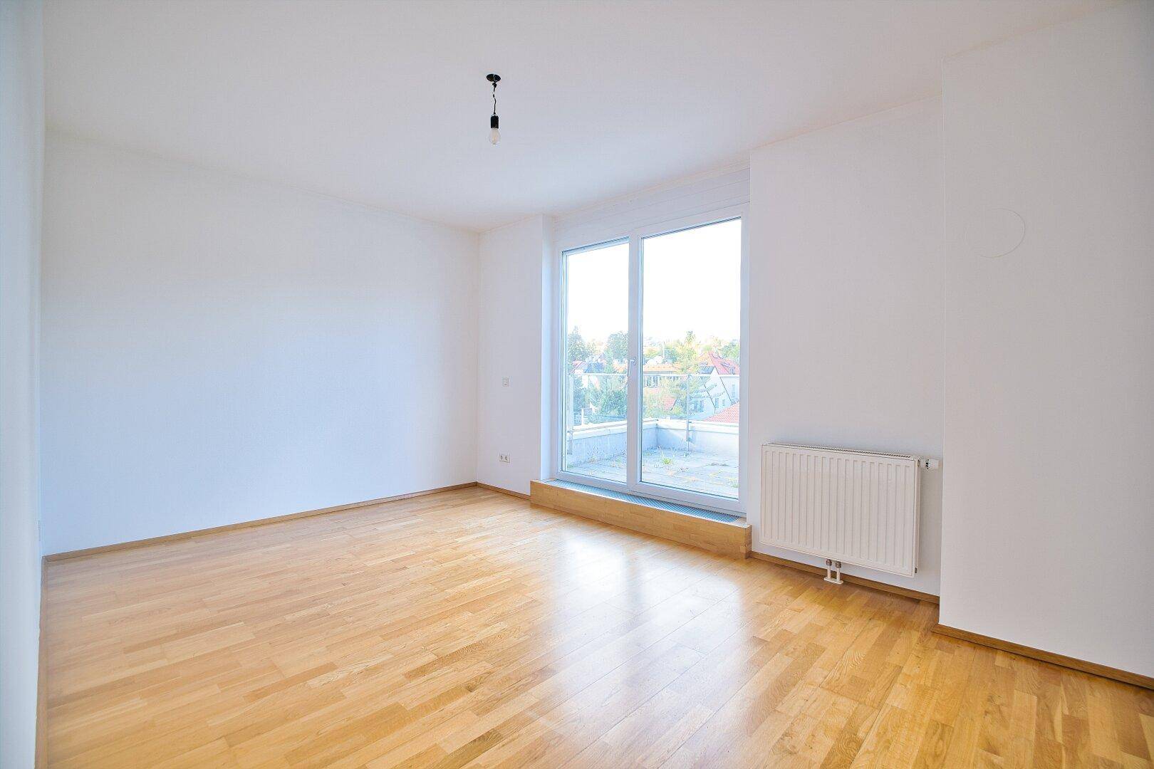 Helles Schlafzimmer mit Parkettboden, weißen Wänden und großem Fenster mit Heizkörper.