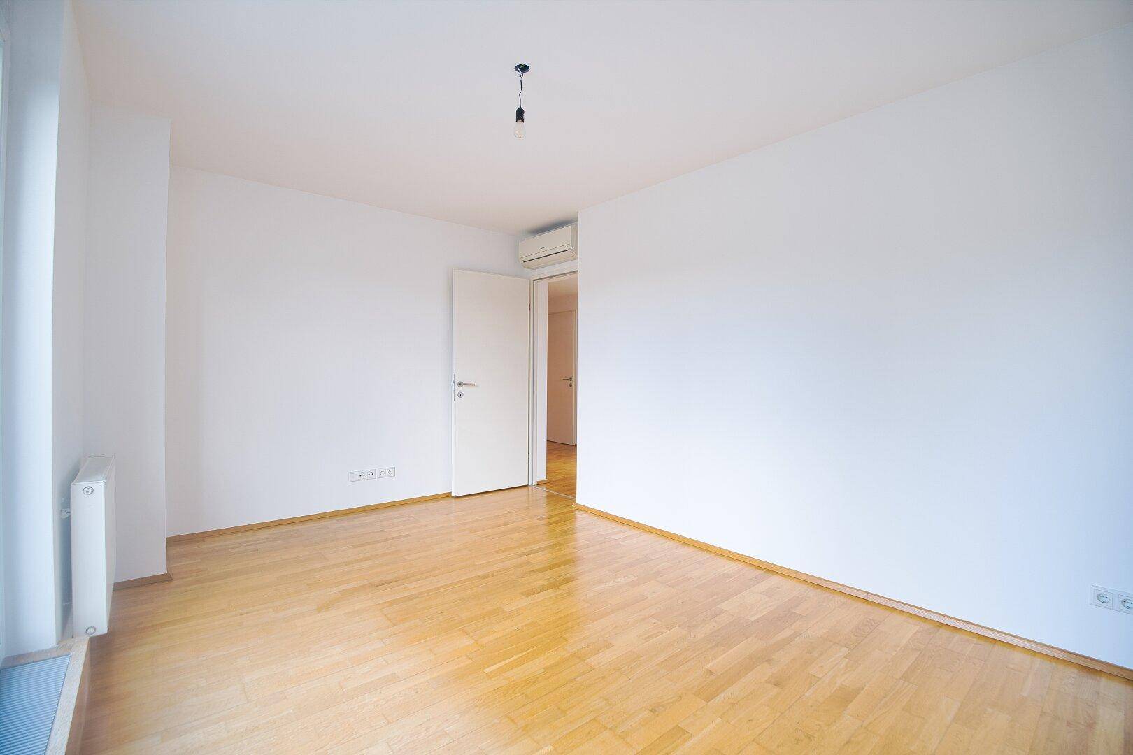 Geräumiges Zimmer mit Parkettboden, weißen Wänden und Zugang zum Flur, ausgestattet mit Klimaanlage.