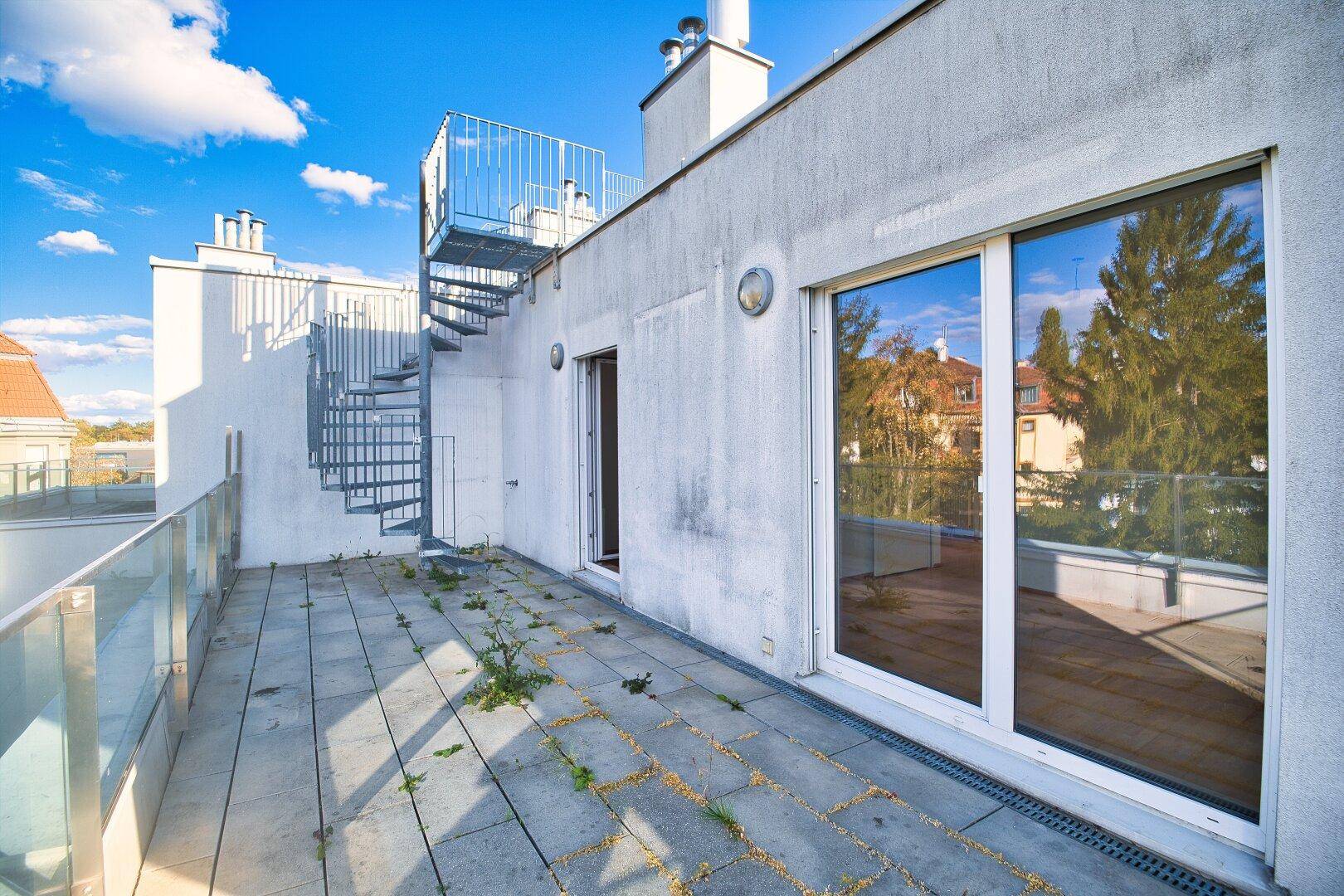 Große Dachterrasse mit Fliesenboden und Zugang zum Innenbereich, inklusive Wendeltreppe.