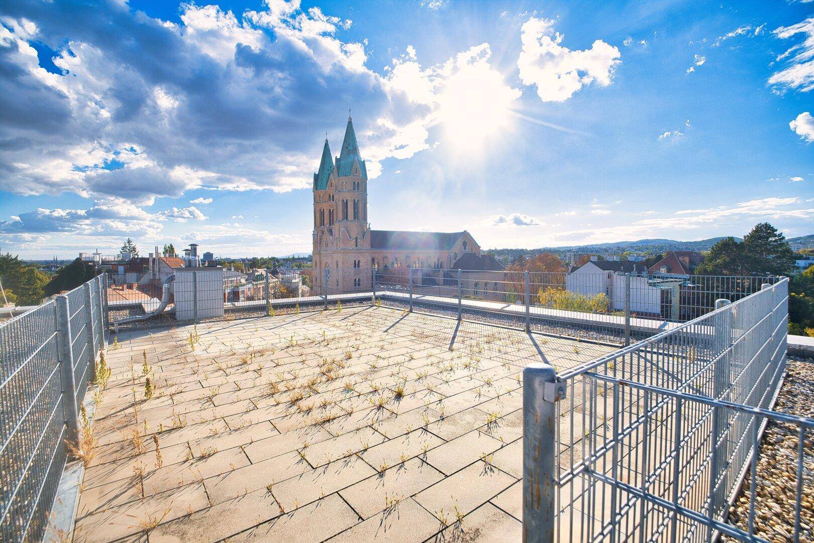 Weitläufige Dachfläche mit Panoramablick auf eine historische Kirche unter strahlendem Himmel.