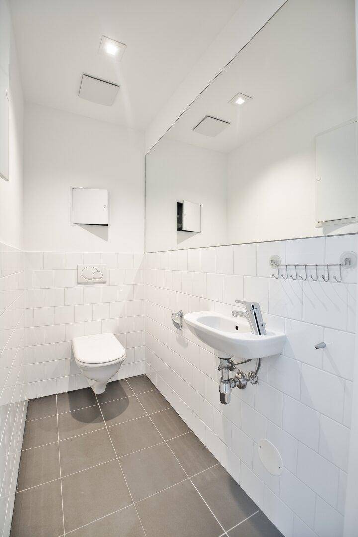 Separates Gäste-WC mit Wand-WC, Waschbecken und großem Spiegel, in minimalistischem Design.