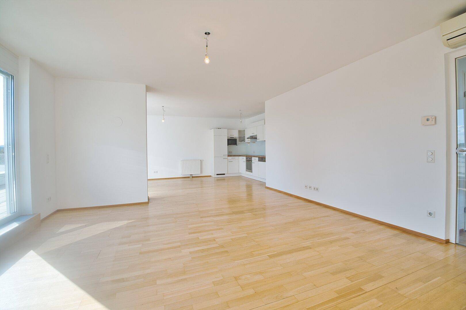 Offener Wohnbereich mit Parkettboden und integrierter Küche im Hintergrund, ideal für modernes Wohnen.
