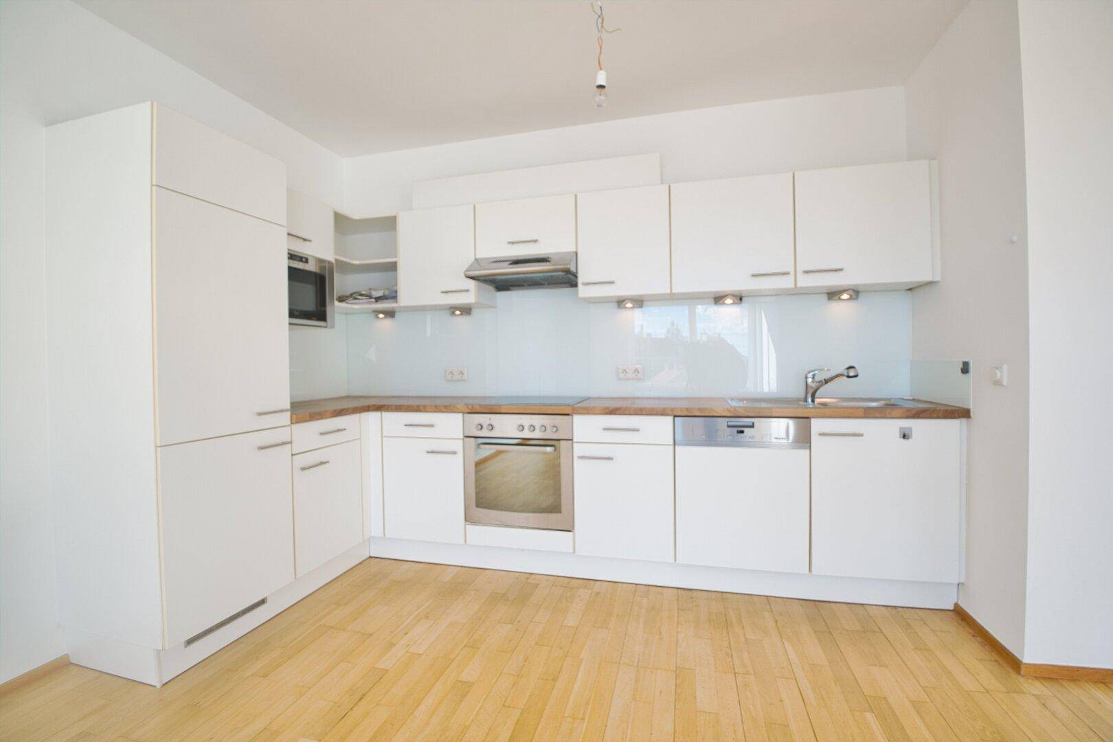 Moderne Einbauküche in Weiß mit Holz-Arbeitsplatte und integrierten Geräten, in neuwertigem Zustand.