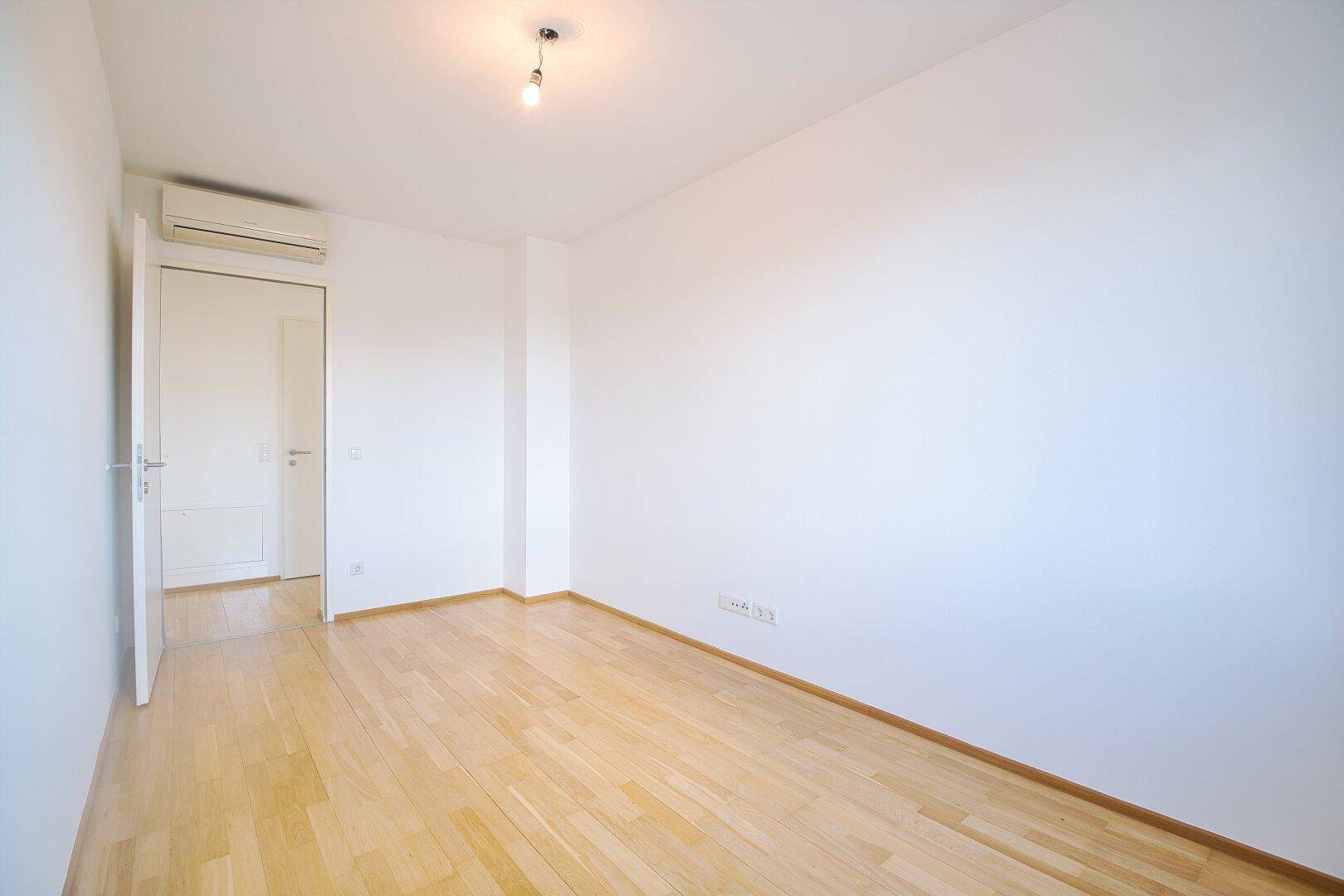 Ruhiges Schlafzimmer mit Parkettboden, weißen Wänden und Klimaanlage für angenehmes Raumklima.