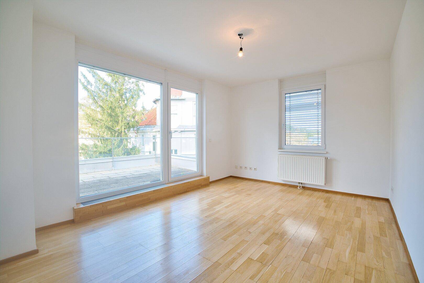 Helles Schlafzimmer mit Parkettboden, großen Fenstern und Zugang zur sonnigen Terrasse.