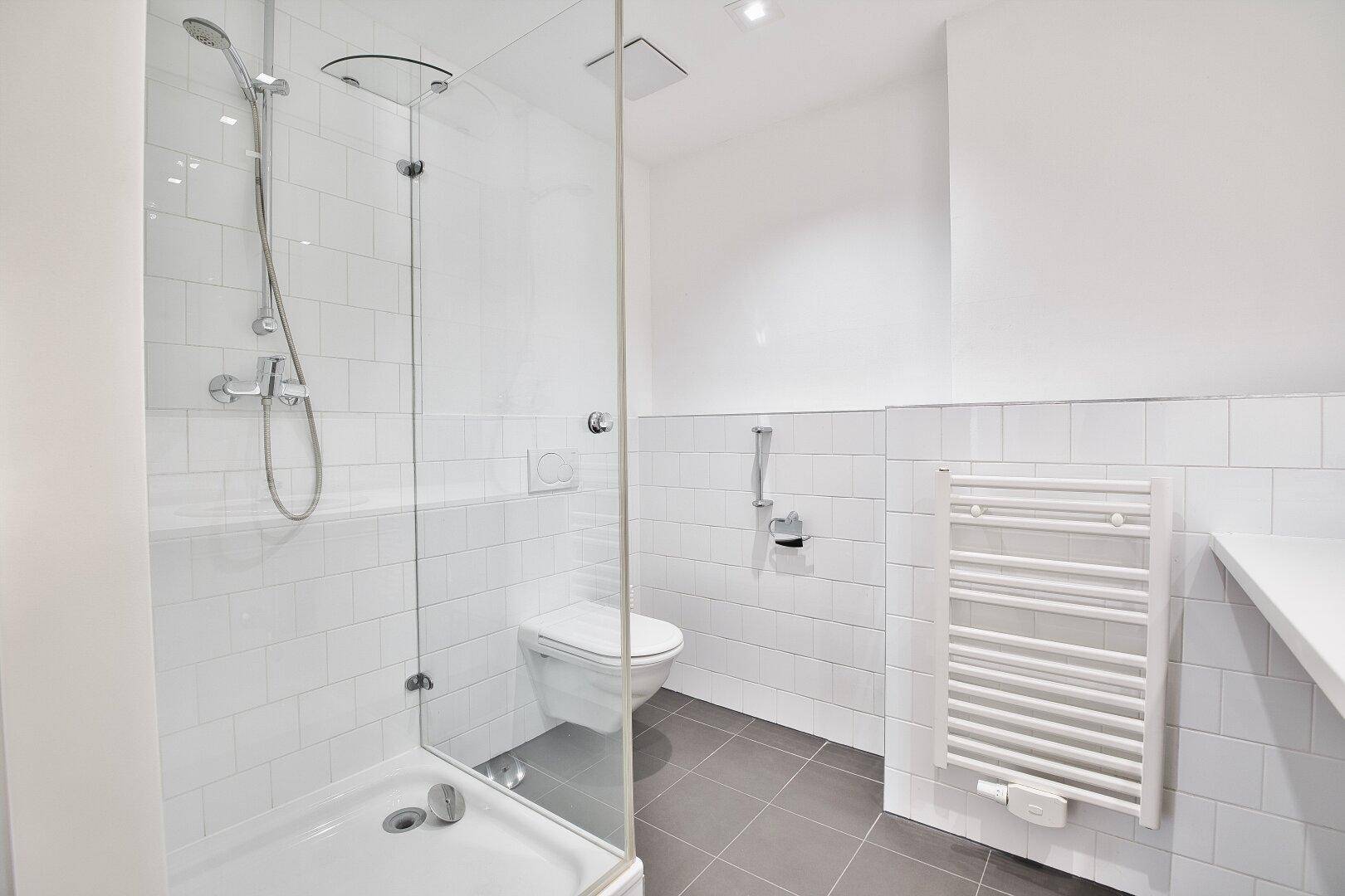 Modernes Badezimmer mit Duschkabine, Wand-WC und beheiztem Handtuchhalter, in hellen Fliesen.