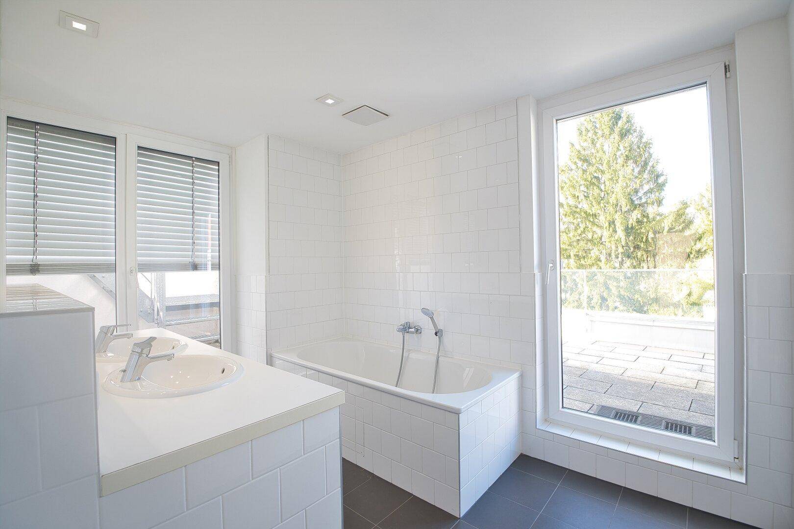 Helles Badezimmer mit Badewanne, Einzelwaschbecken und großem Fenster, bietet viel Tageslicht.