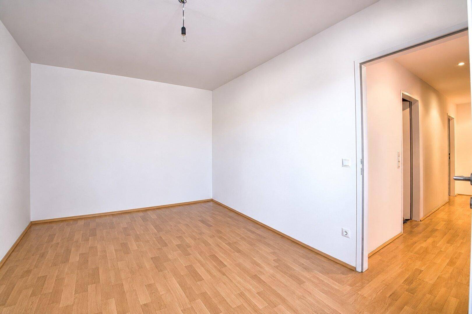 Geräumiger, leerer Raum mit hellem Parkettboden und weiß gestrichenen Wänden, ideal als Schlafzimmer.