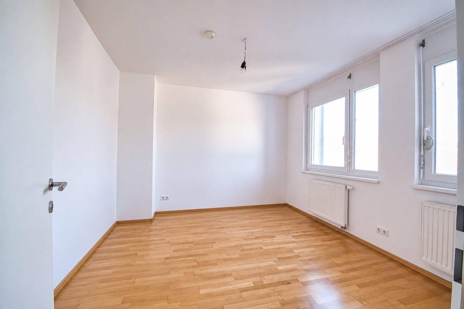Helles, unmöbliertes Zimmer mit Parkettboden und zwei Fenstern, ideal als Schlaf- oder Arbeitszimmer.