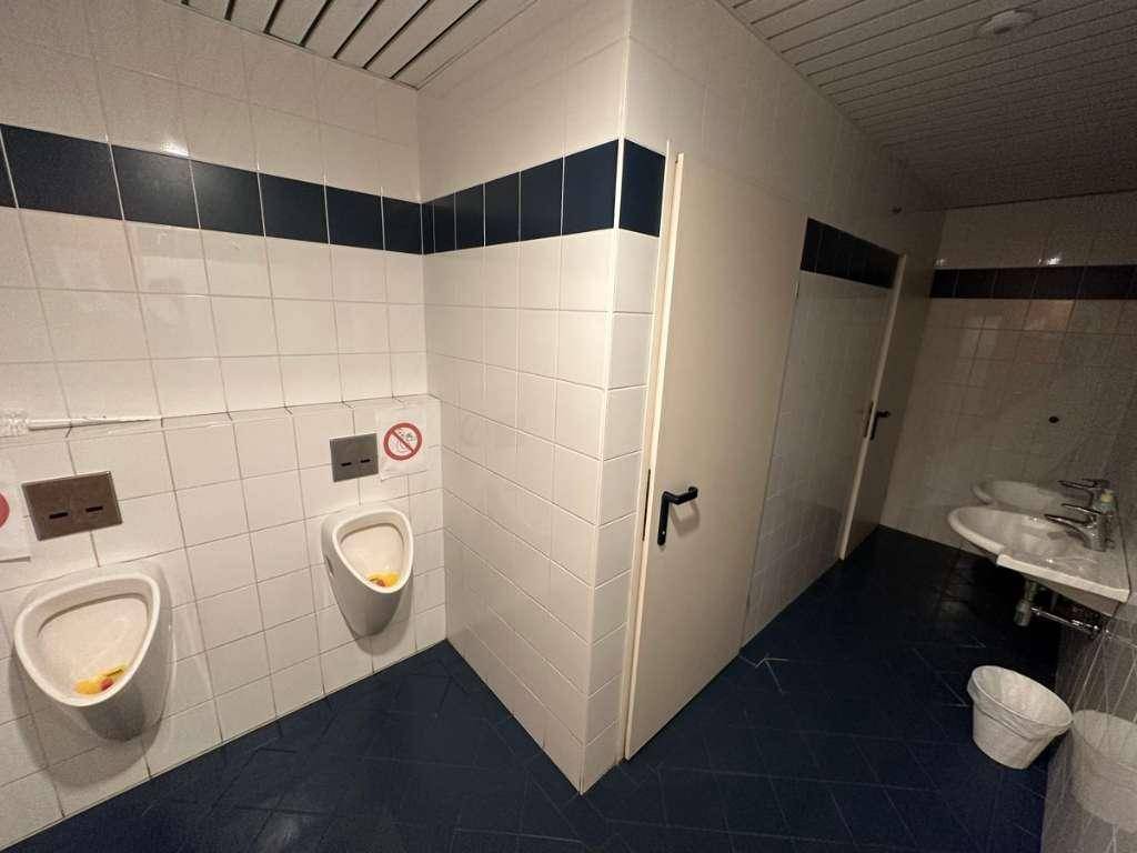 Funktionaler öffentlicher Toilettenraum mit Urinalen, Waschbecken und weißen Fliesenwänden.