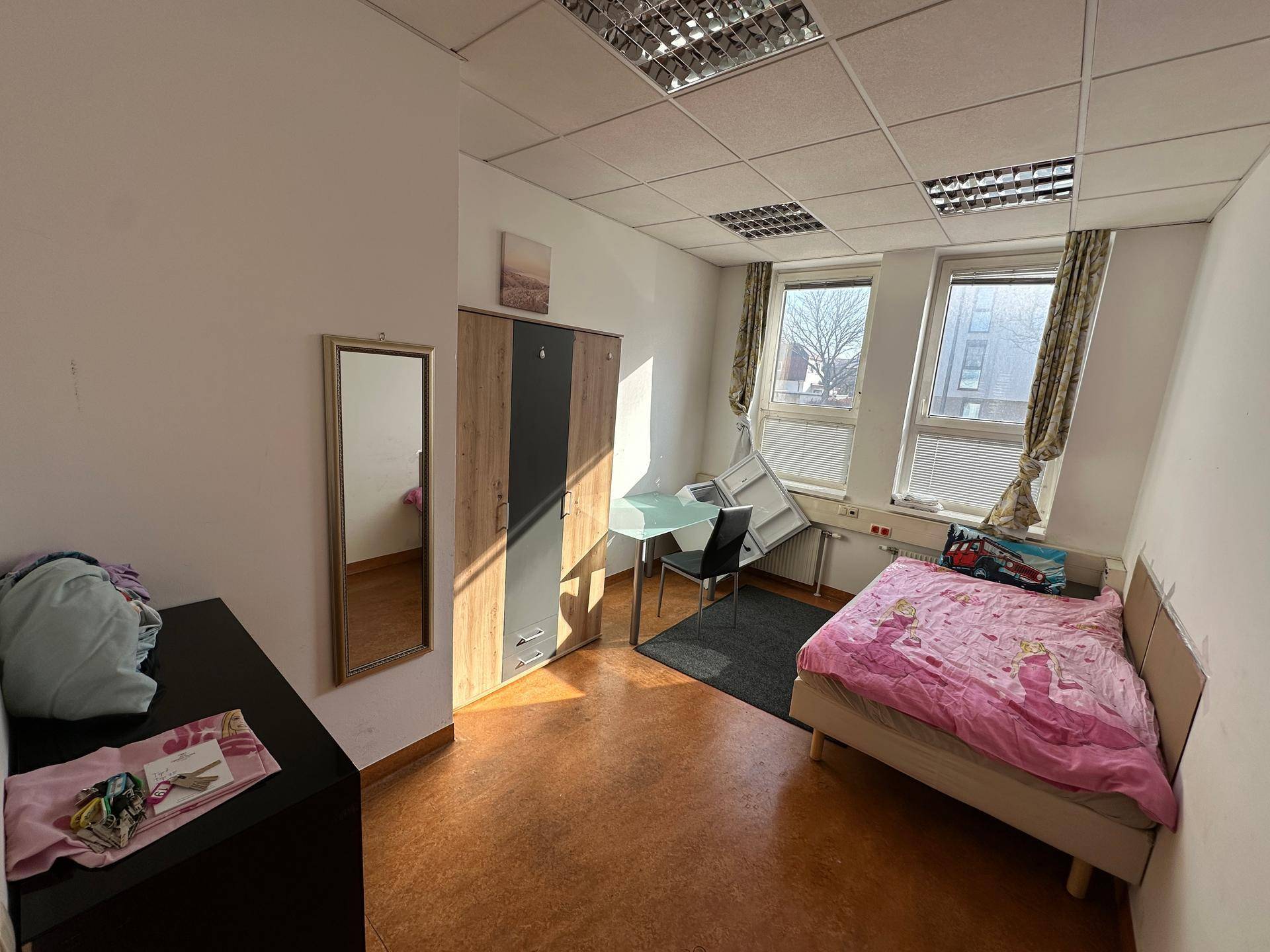 Lichtdurchflutetes Zimmer mit Bett, Schreibtisch und Kleiderschrank, ausgestattet mit Laminatboden.