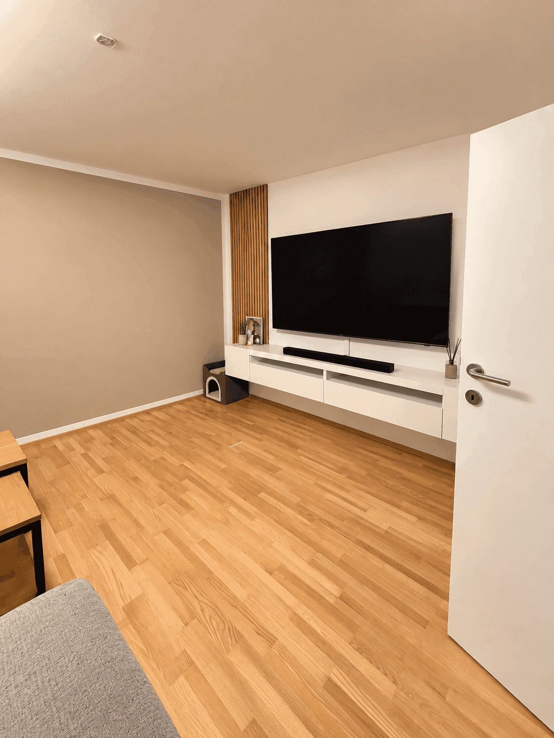 Modernes Wohnzimmer mit Holzboden, Wandfernseher und schlichter Dekoration.