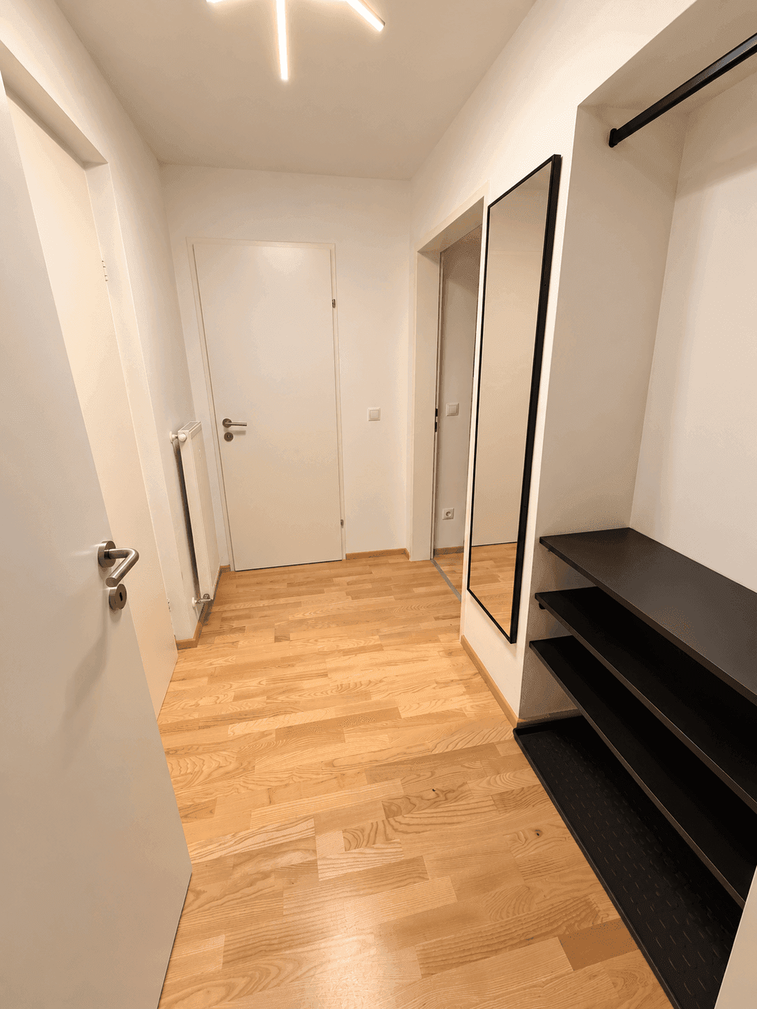 Heller Flur mit Holzboden, Ganzkörperspiegel und offener Garderobe.