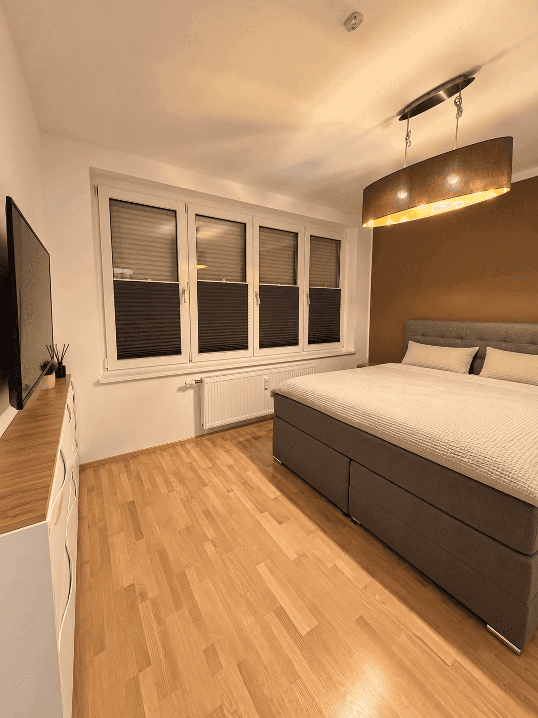 Gemütliches Schlafzimmer mit Doppelbett, Holzboden und Fenster mit Jalousien.