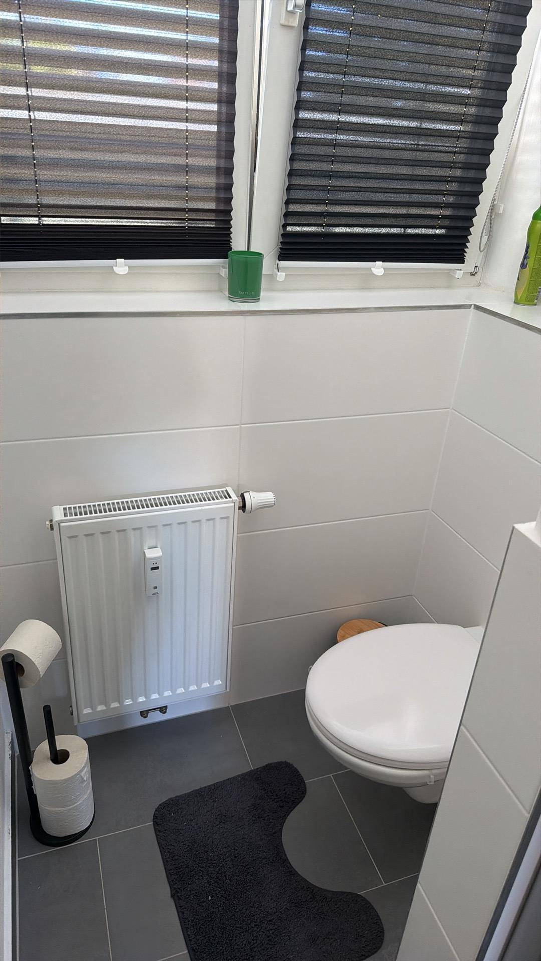Separate Toilette mit Fenster, Heizung und dunklen Bodenfliesen.