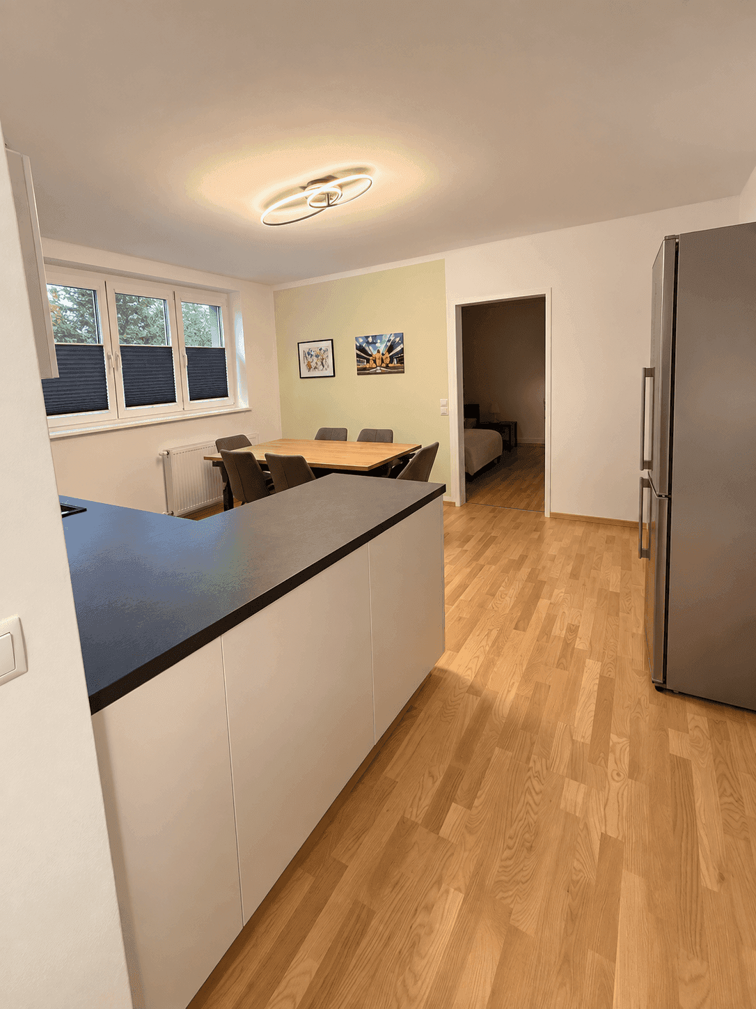 Moderne Küche mit Essbereich, Holzboden und Blick in ein angrenzendes Schlafzimmer.