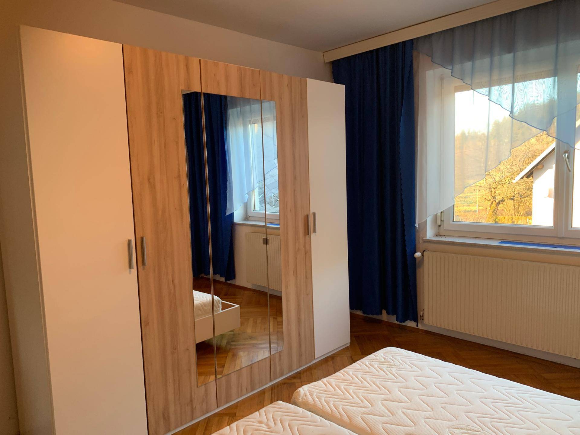 Schlafzimmer mit großem Kleiderschrank, Doppelbett und einem Fenster mit blauen Vorhängen.