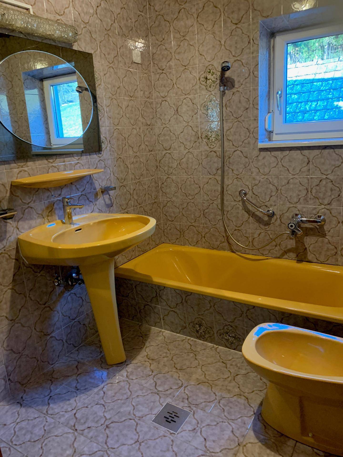 Badezimmer mit gelben Sanitärobjekten, gemusterten Fliesen und einem Fenster für Tageslicht.