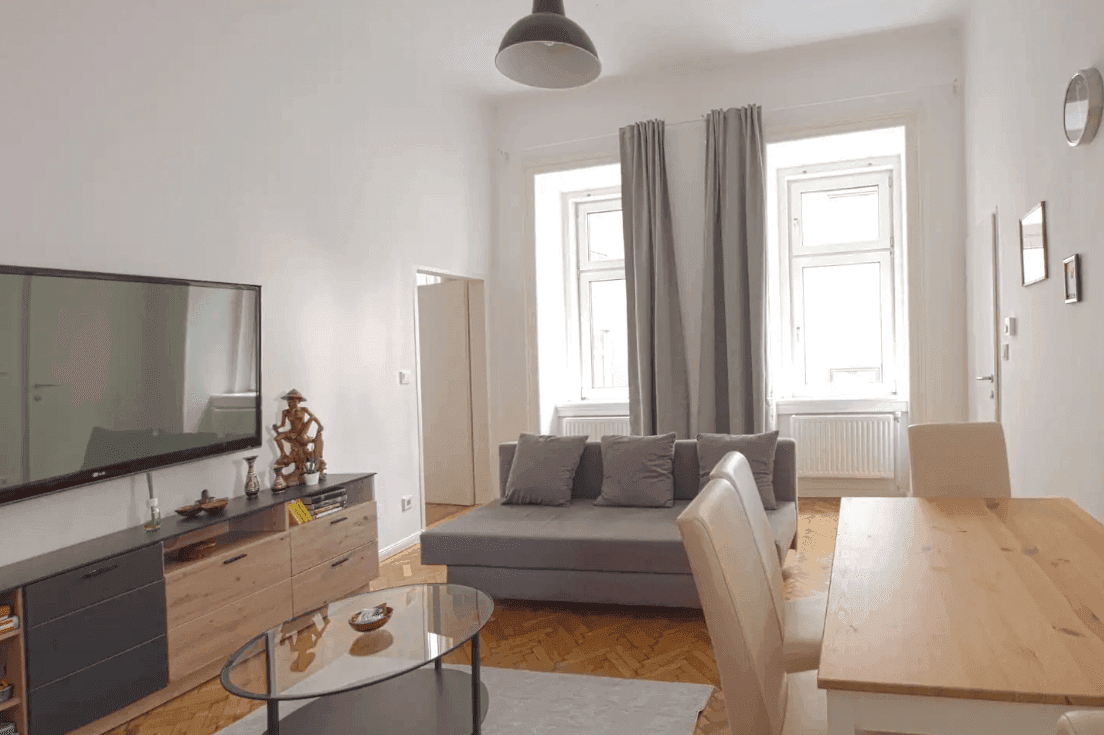 Geräumiges Wohnzimmer mit Parkettboden, großen Fenstern und einem Essbereich.