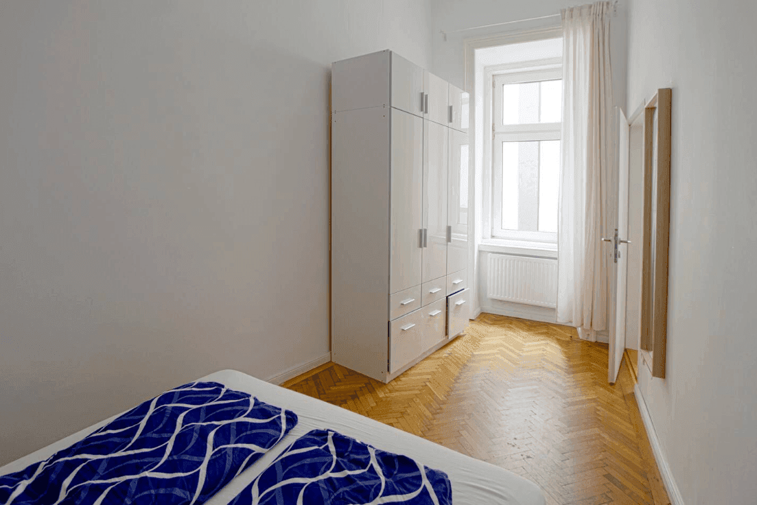 Schlafzimmer mit Parkettboden, großem Kleiderschrank und Fenster für Tageslicht.