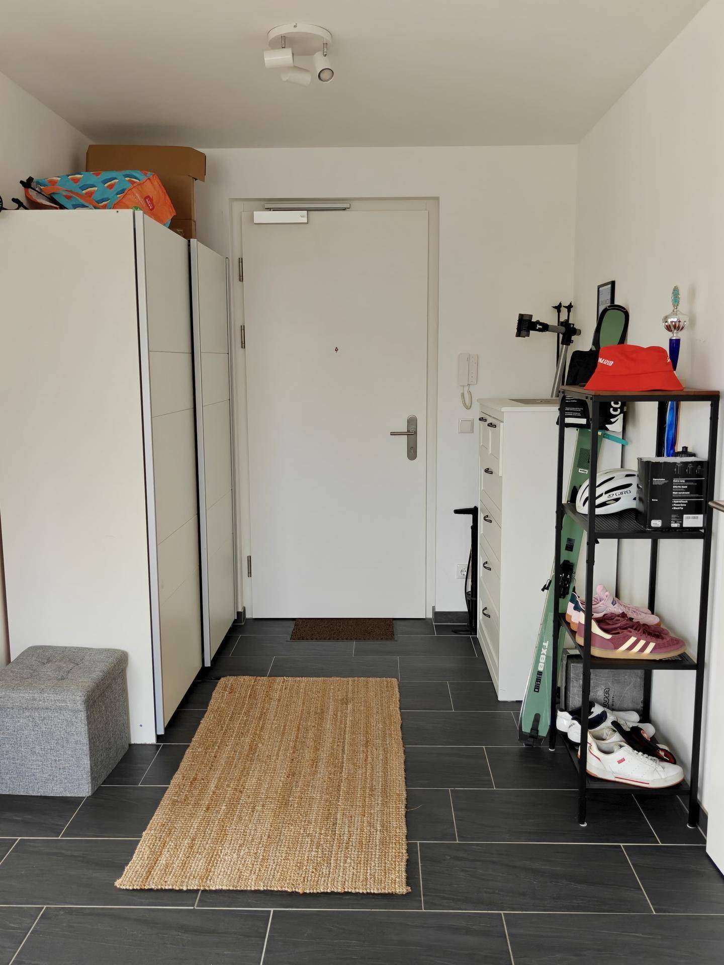 Heller Eingangsbereich mit dunklen Fliesen, praktischen Schuhregalen und Garderobenschrank.
