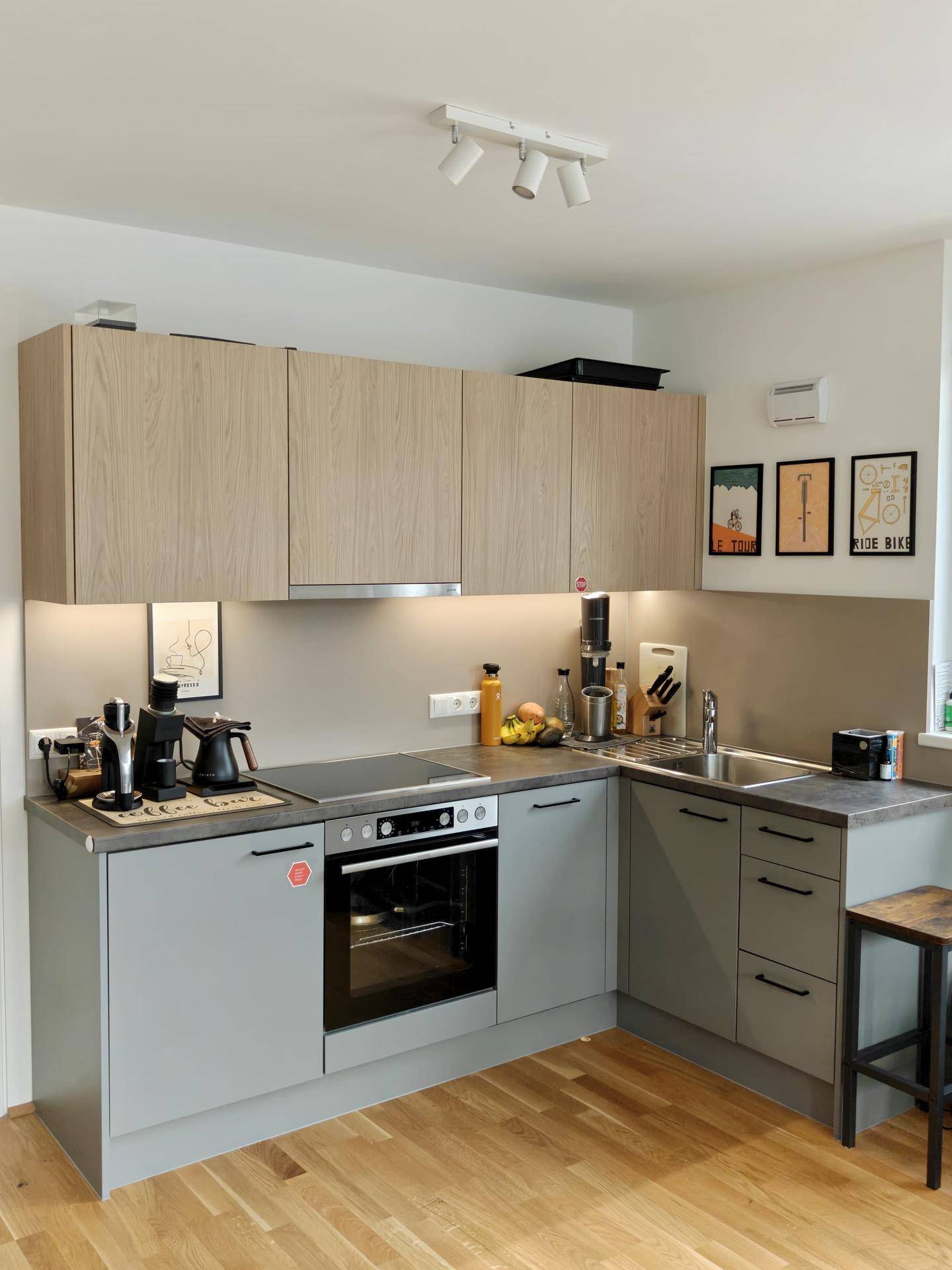 Moderne Einbauküche mit hellen Holz- und grauen Fronten sowie integrierten Geräten und Kochfeld.
