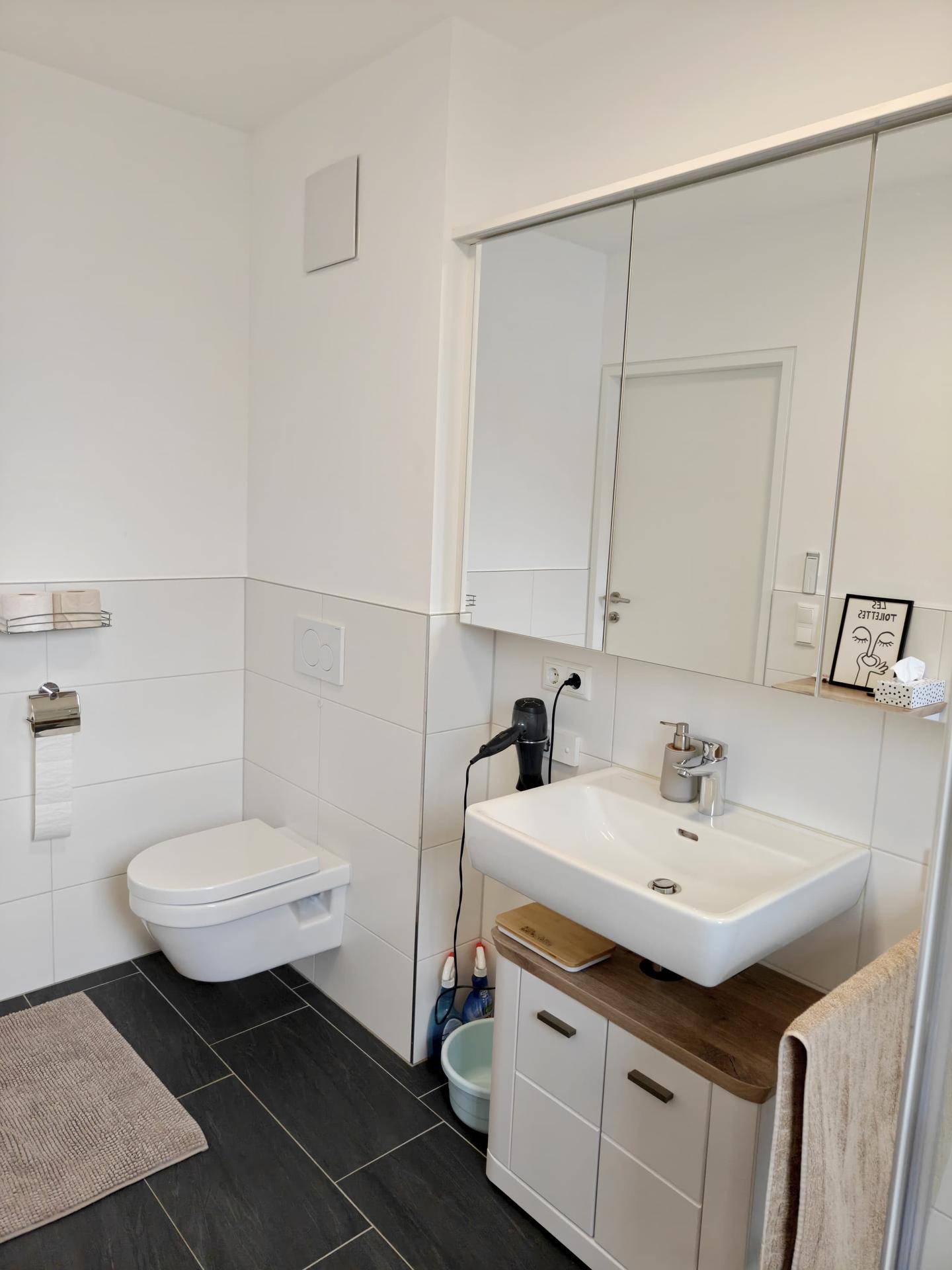 Helles Badezimmer mit wandhängendem WC, Einzelwaschbecken und Spiegelschrank für zusätzlichen Stauraum.