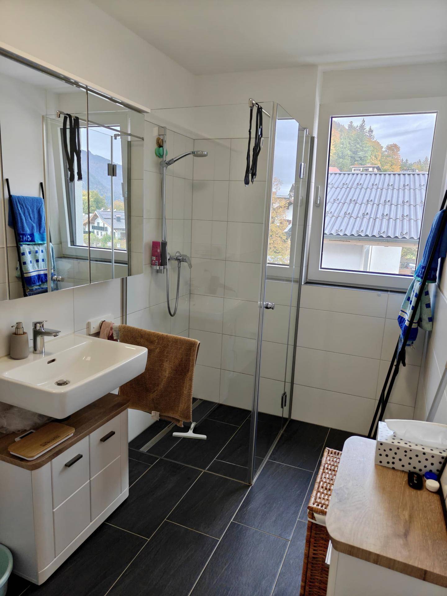 Modernes Badezimmer mit begehbarer Dusche, Fenster und dunklen Bodenfliesen für ein frisches Ambiente.
