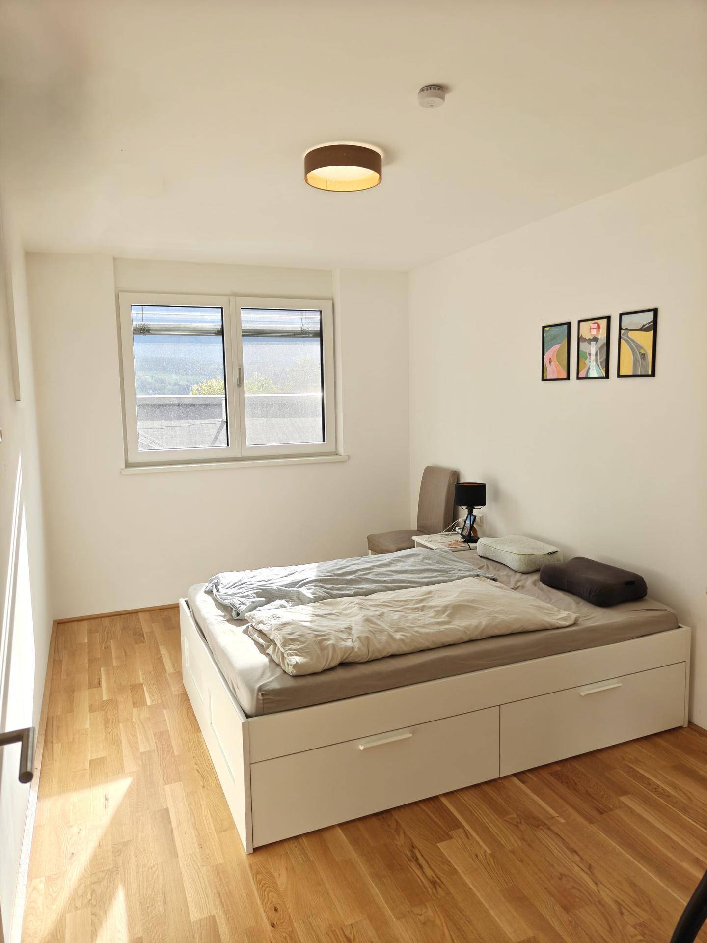 Schlafzimmer mit Holzboden, großem Fenster und praktischem Bett mit integriertem Stauraum.