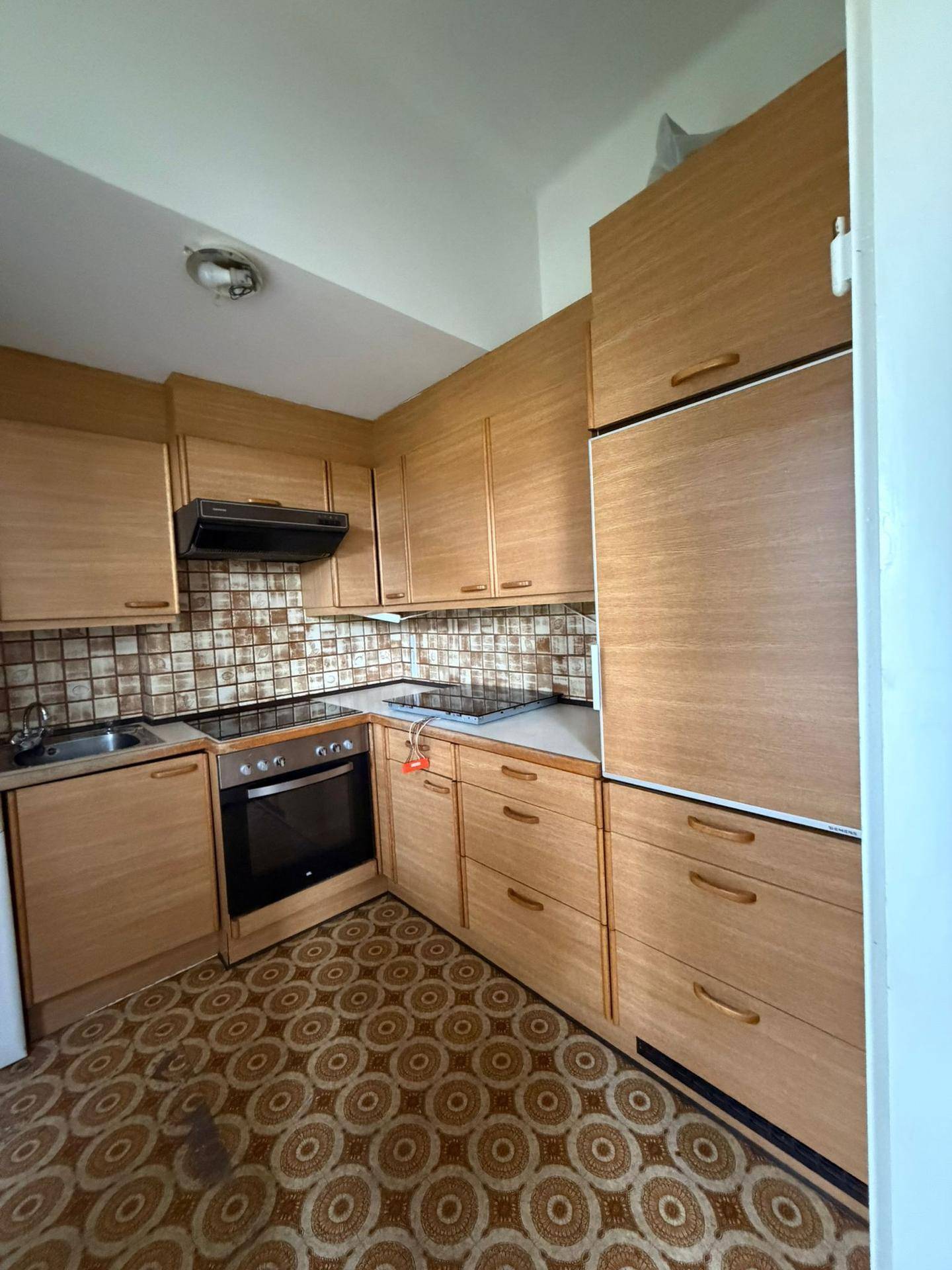 Traditionelle Küche mit Holzschränken, gemusterten Fliesen und Einbaugeräten, inklusive Backofen und Kochfeld.