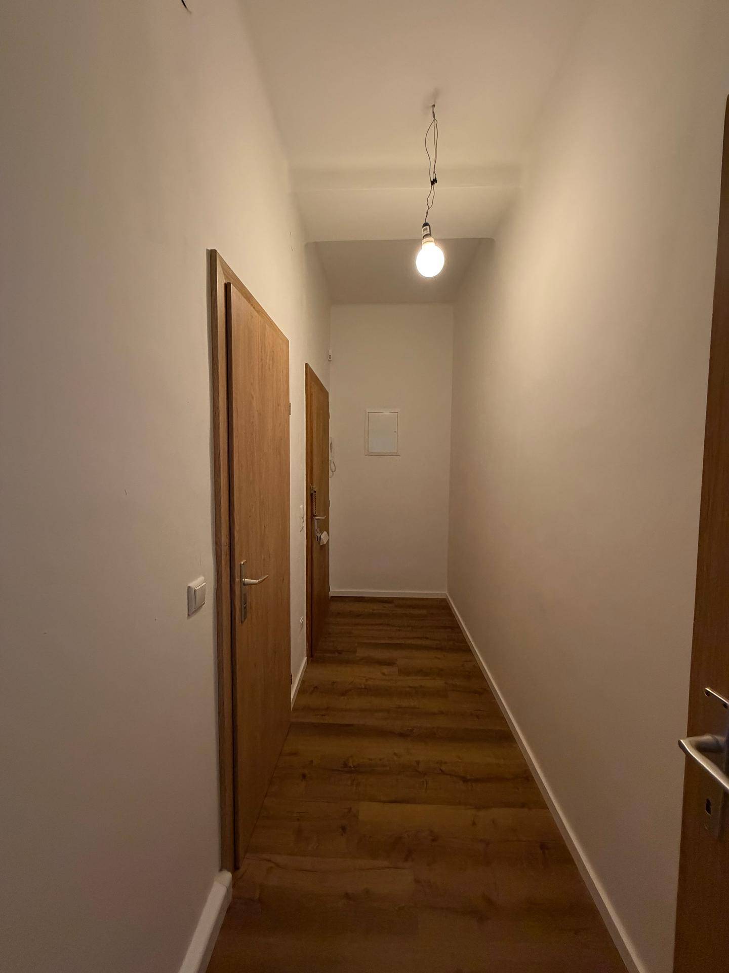 Schmaler Flur mit Laminatboden und weißen Wänden, der eine klare Durchgangsfläche bietet.