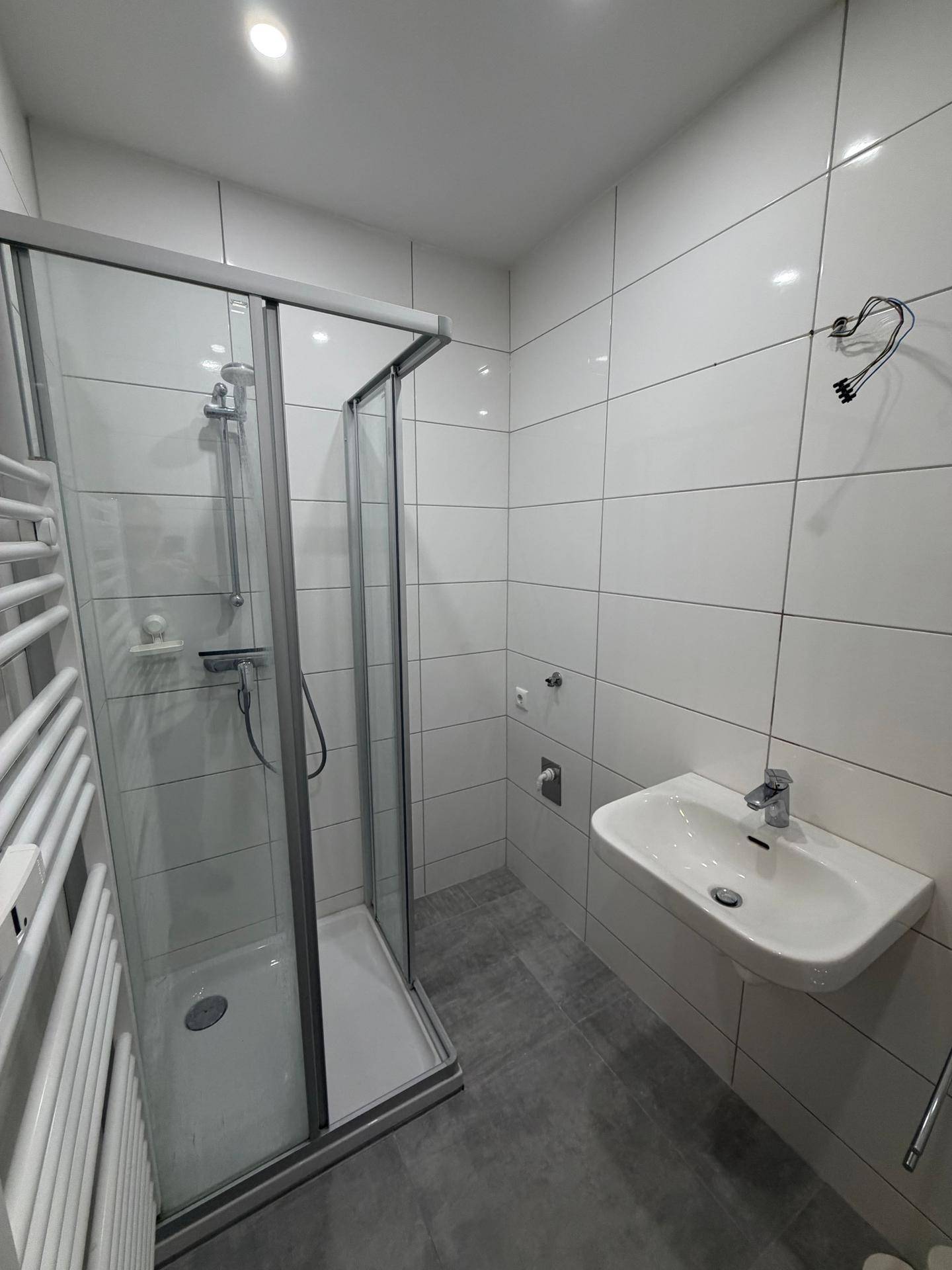 Modernes Badezimmer mit Duschkabine, Waschbecken und beheiztem Handtuchhalter, hell gefliest.