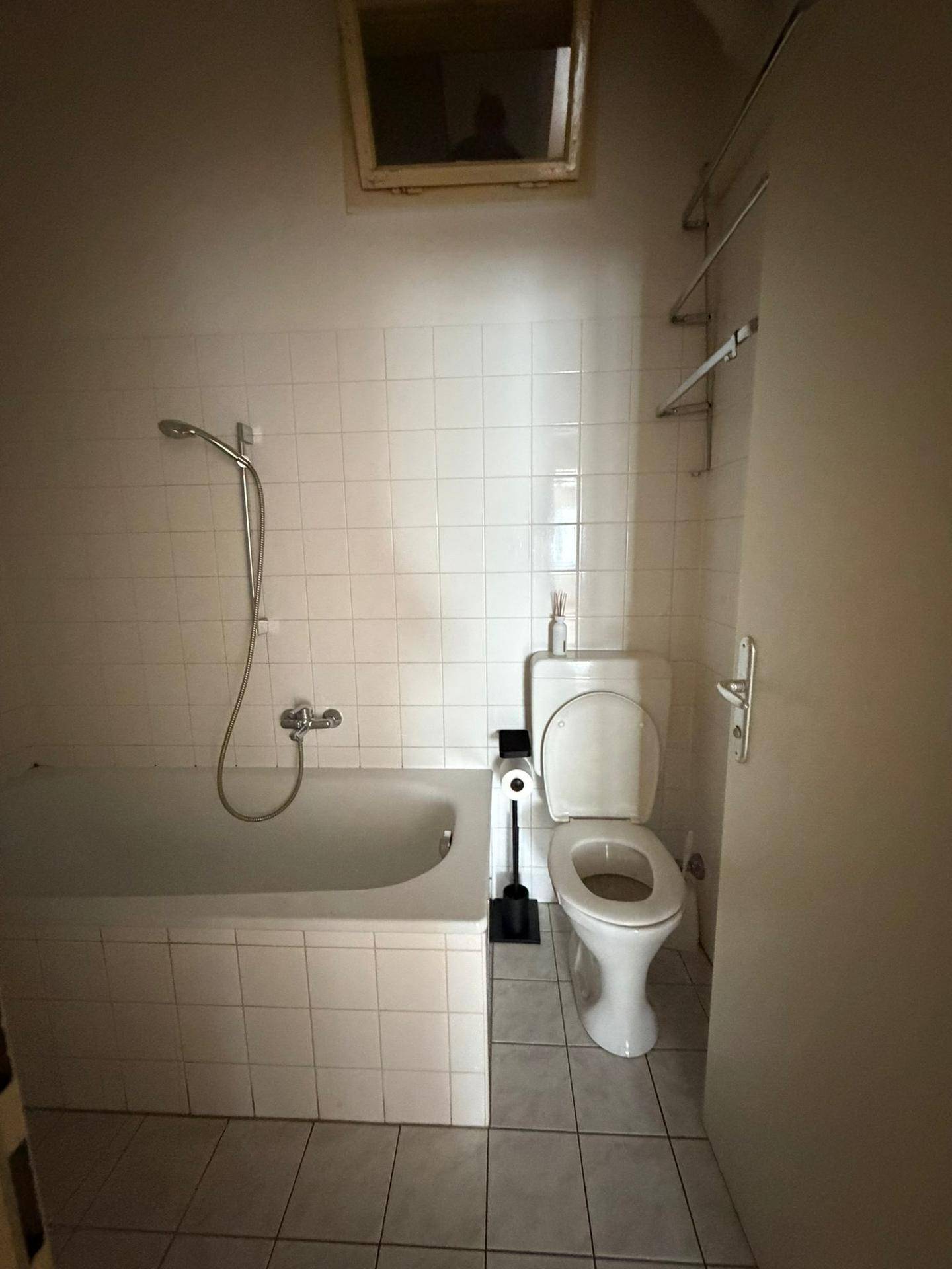 Funktionales Badezimmer mit Badewanne, Duscharmatur und Toilette, komplett gefliest in Weiß.