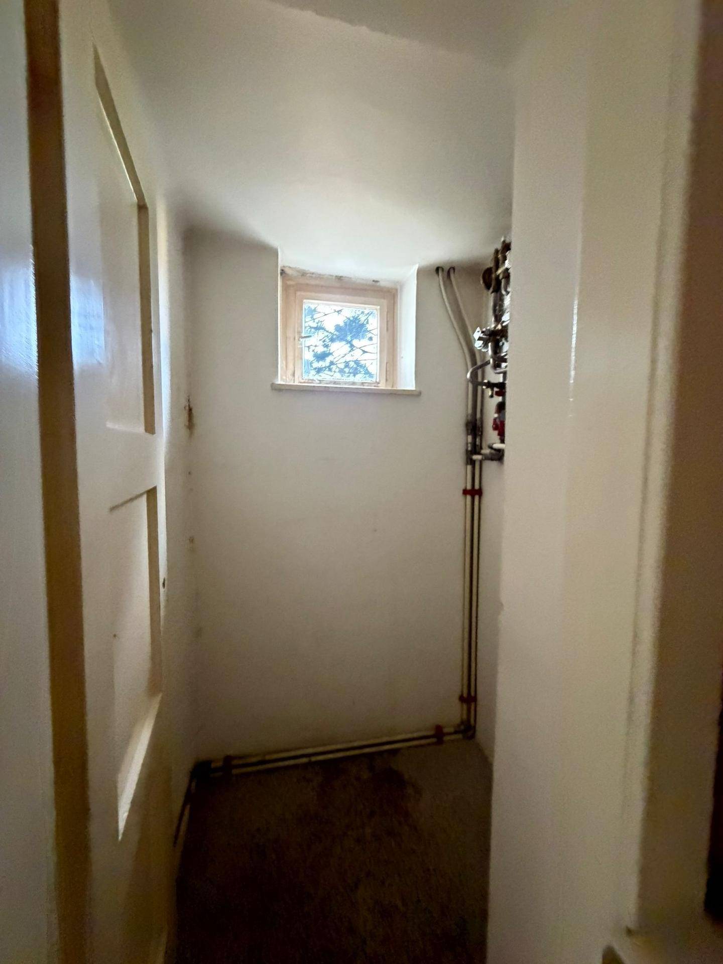 Kleiner Hauswirtschaftsraum im Untergeschoss mit Fenster und sichtbaren Rohrleitungen.