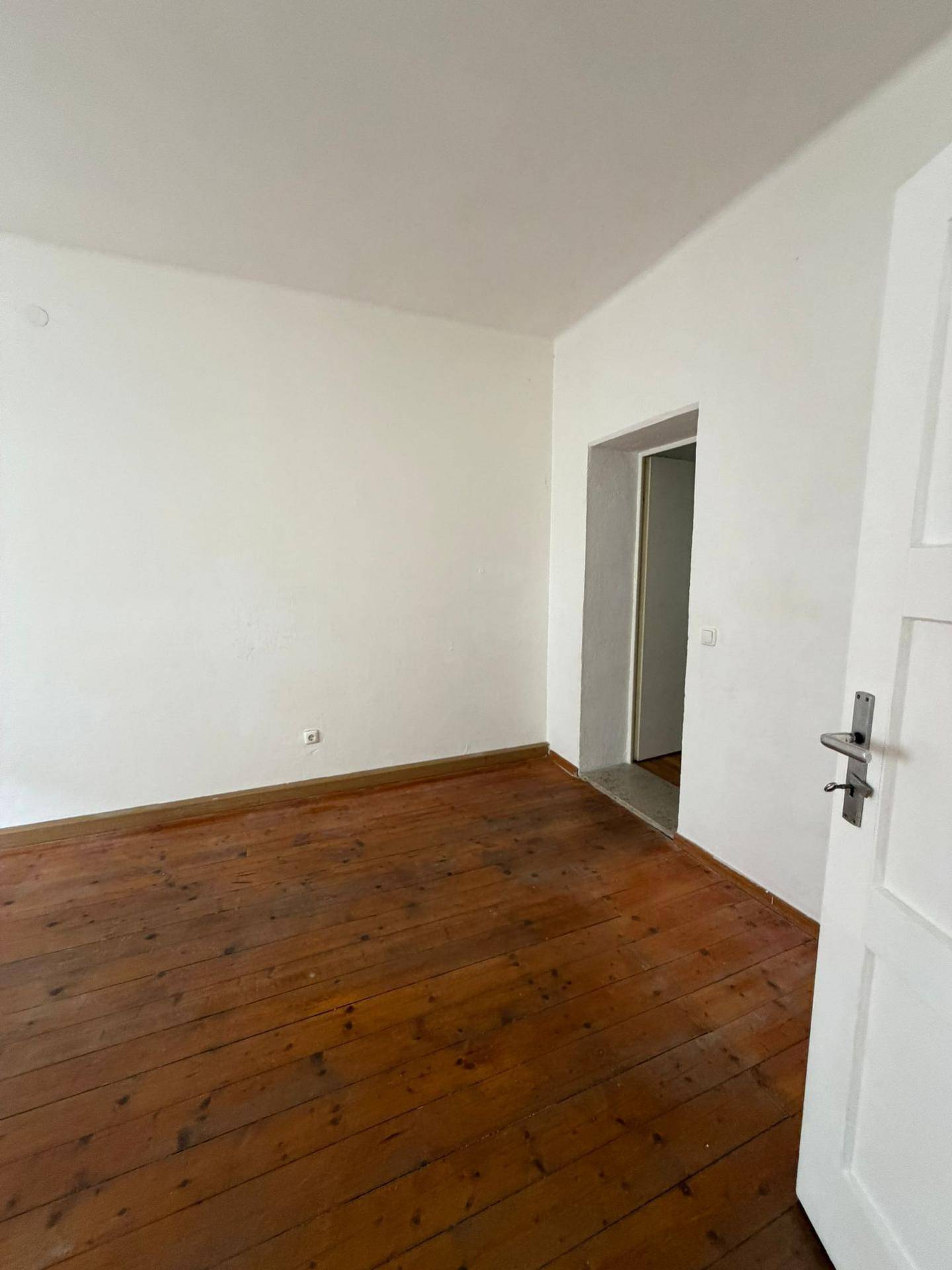 Leeres Zimmer mit Dielenboden und weiß gestrichenen Wänden, bereit zur individuellen Gestaltung.