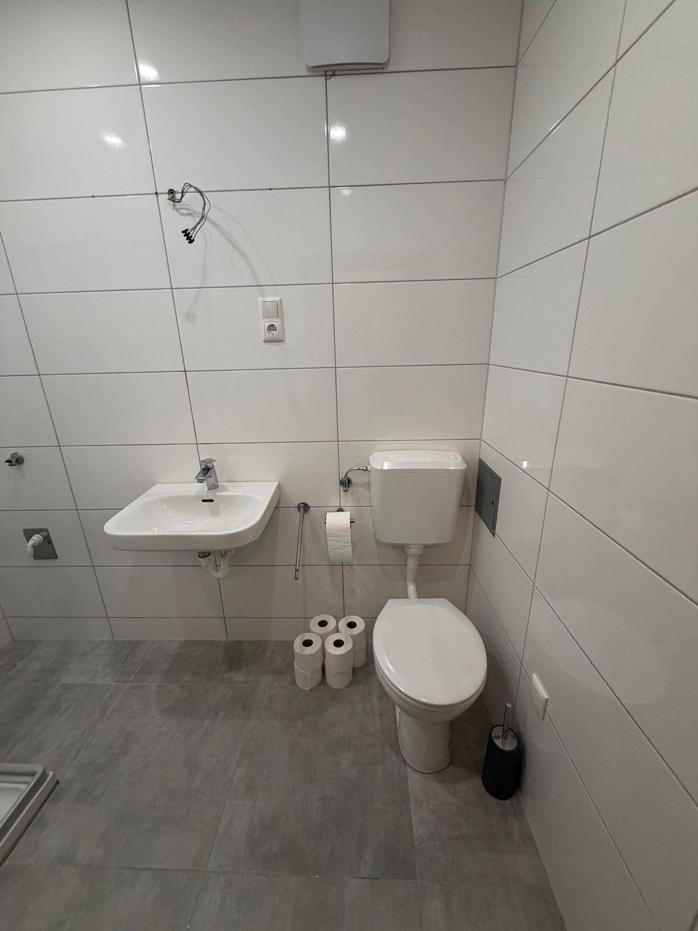Helles Badezimmer mit WC und Waschbecken, ausgestattet mit modernen weißen Wandfliesen.