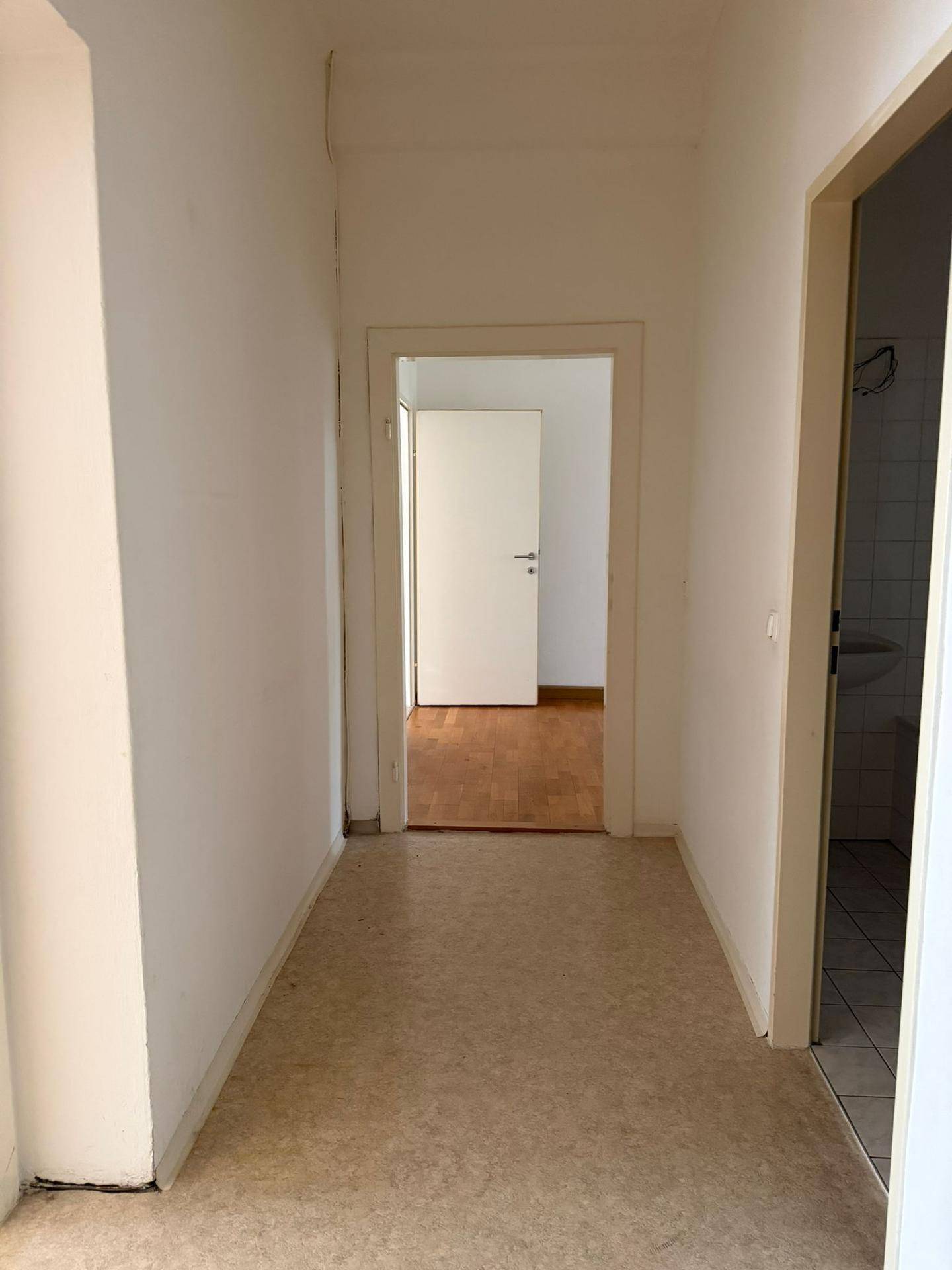 Heller Flur mit Linoleumboden und weißen Wänden, verbindet verschiedene Zimmer der Wohnung.