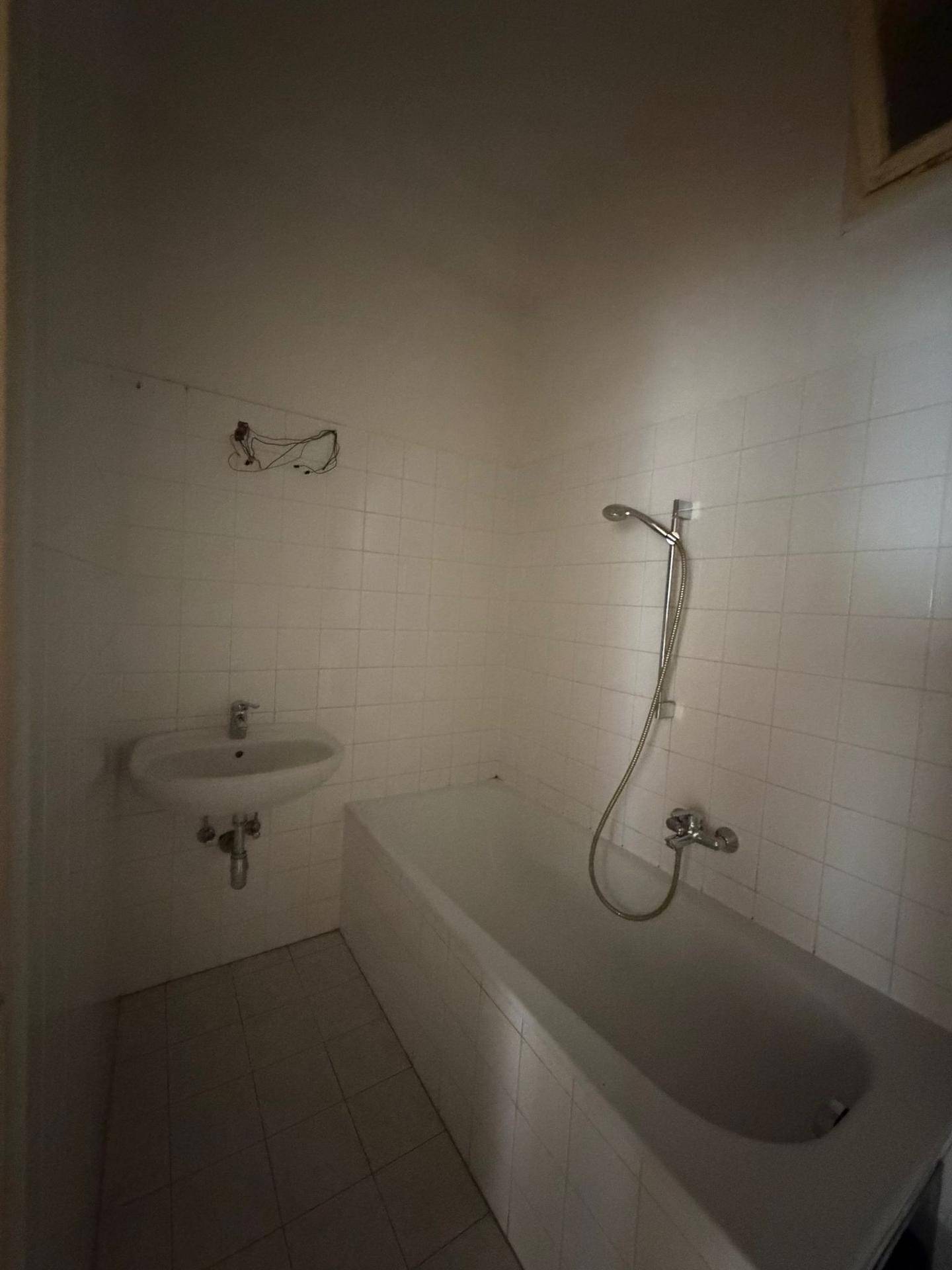Einfaches Badezimmer mit Badewanne, Duscharmatur und Waschbecken, komplett gefliest in Weiß.